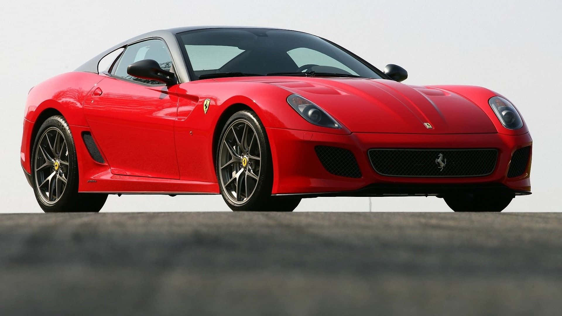 Ferrari 599 Gtb Fiorano 桌布 壁紙 — 一輛時尚的紅色法拉利跑車，帶有黑色飾邊和金色輪圈，停在灰色表面上，背景是淡色的天空。