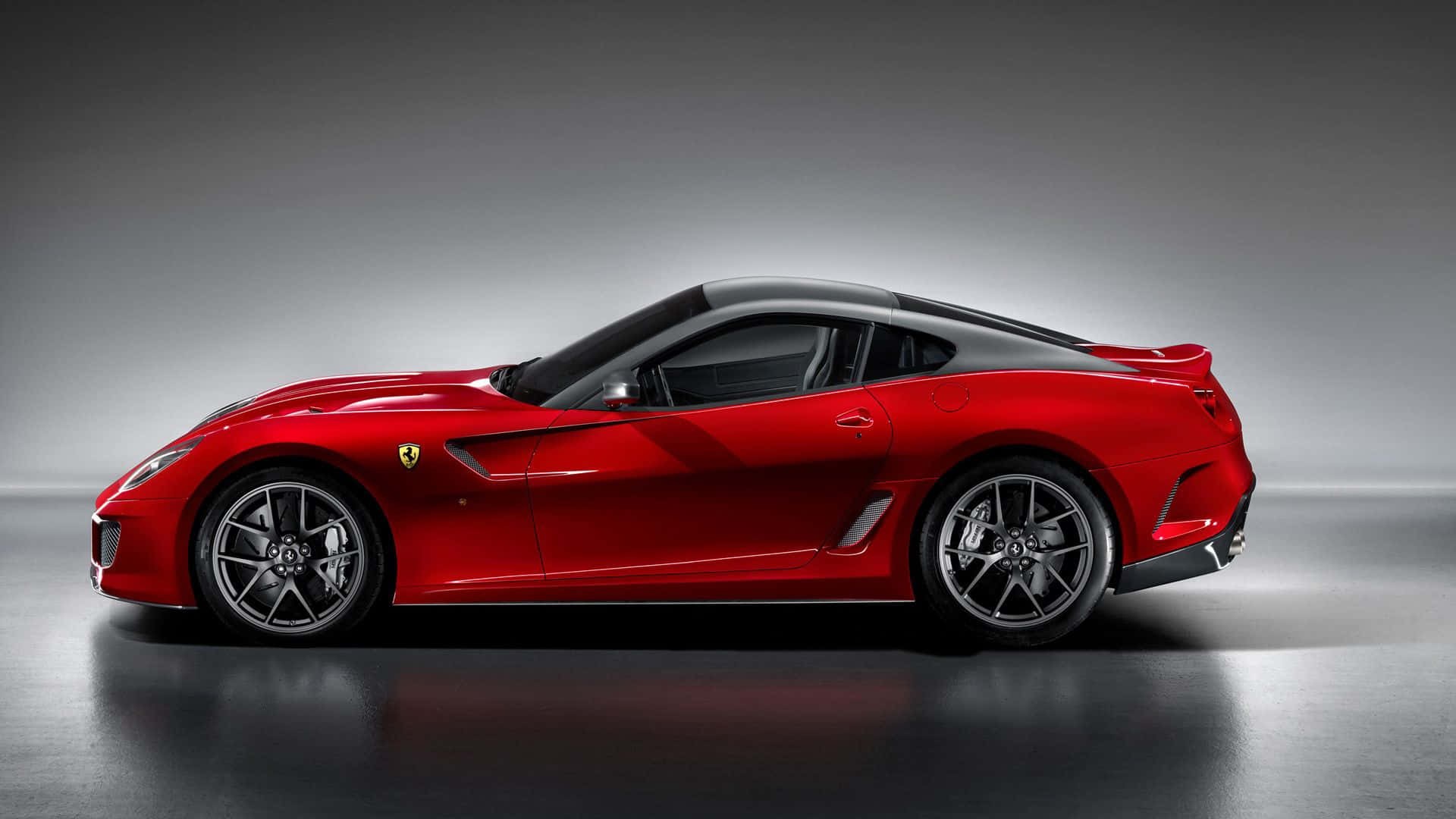Ferrari 599 Gtb Fiorano 桌布 壁紙 — 一輛時尚的紅色法拉利跑車，配備黑色車頂和銀色輪圈，矗立在極簡風格的攝影棚中，地板反射光線，背景為灰色漸變。