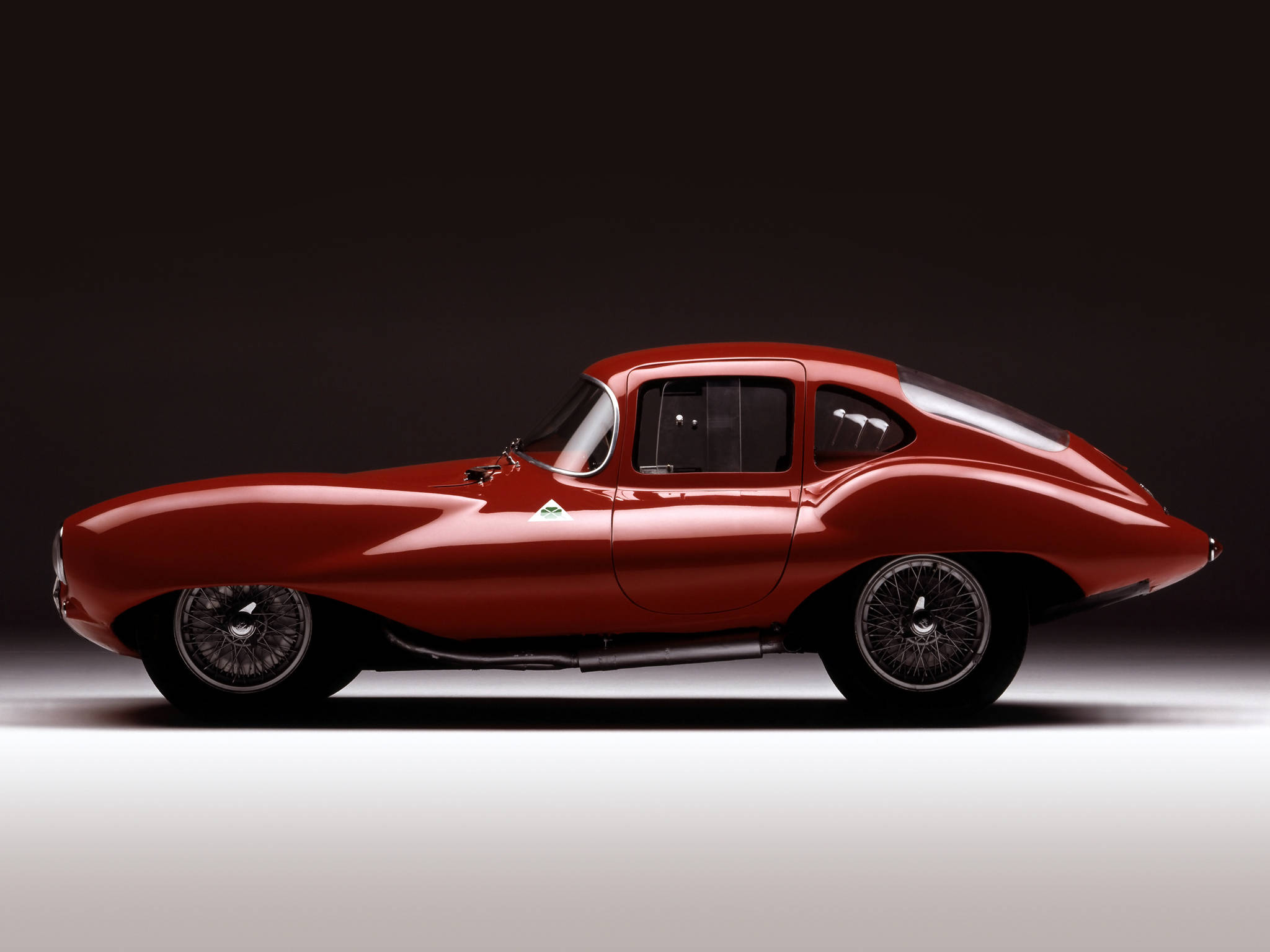 alfa romeo iPhone 桌布 壁紙 — 一輛時尚的紅色經典跑車在黑暗的攝影棚背景下以側面姿態滑行，配以戲劇性燈光。
