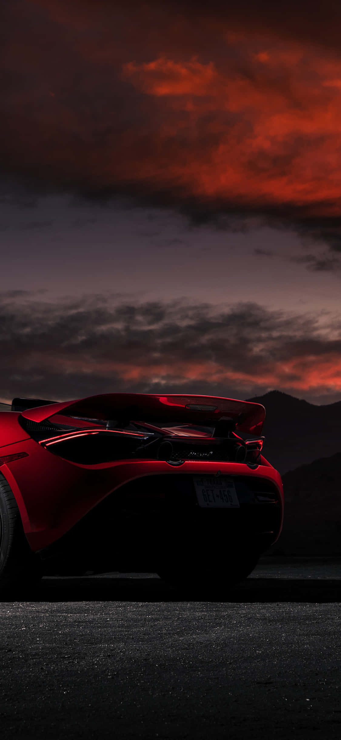 iPhone Xs Mclaren 720s 桌布 壁紙 — 一輛時尚的紅色跑車剪影在火熱的橙色和紫色日落天空下，映襯著遠山閃耀。