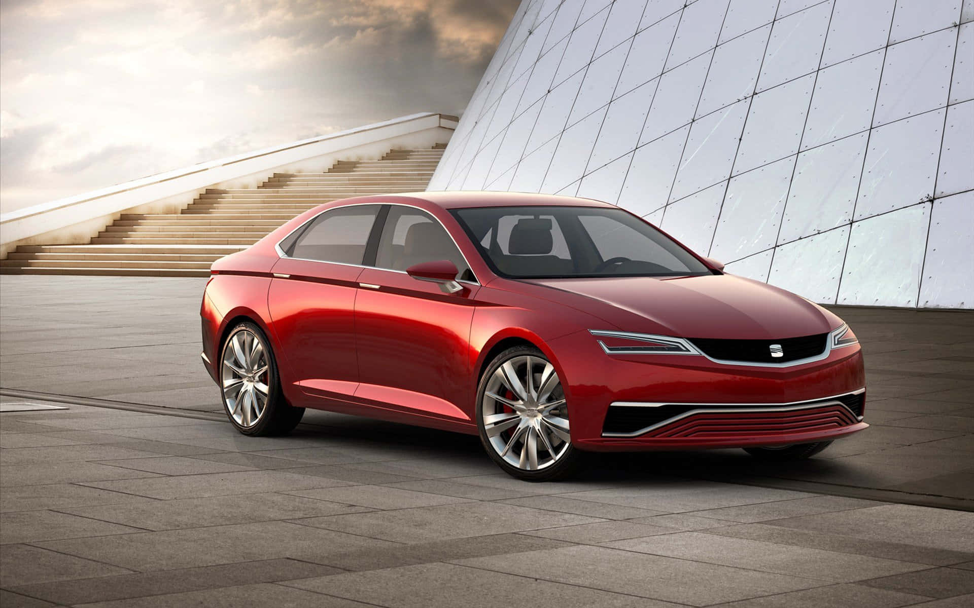 seat 桌布 壁紙 — 一輛時尚的紅色轎車在柔和日光下閃閃發光，旁邊是帶有幾何樓梯和反光玻璃牆的現代建築。
