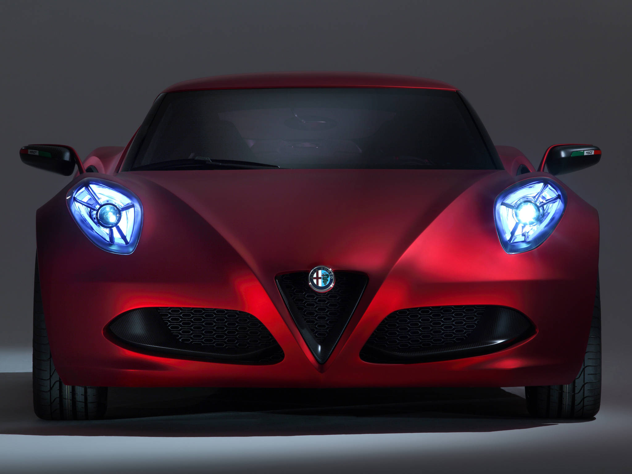 alfa romeo iPhone 桌布 壁紙 — 一輛時尚的紅色阿爾法羅密歐跑車，配備發光的藍色頭燈，在黑暗的攝影棚背景下向前凝視。