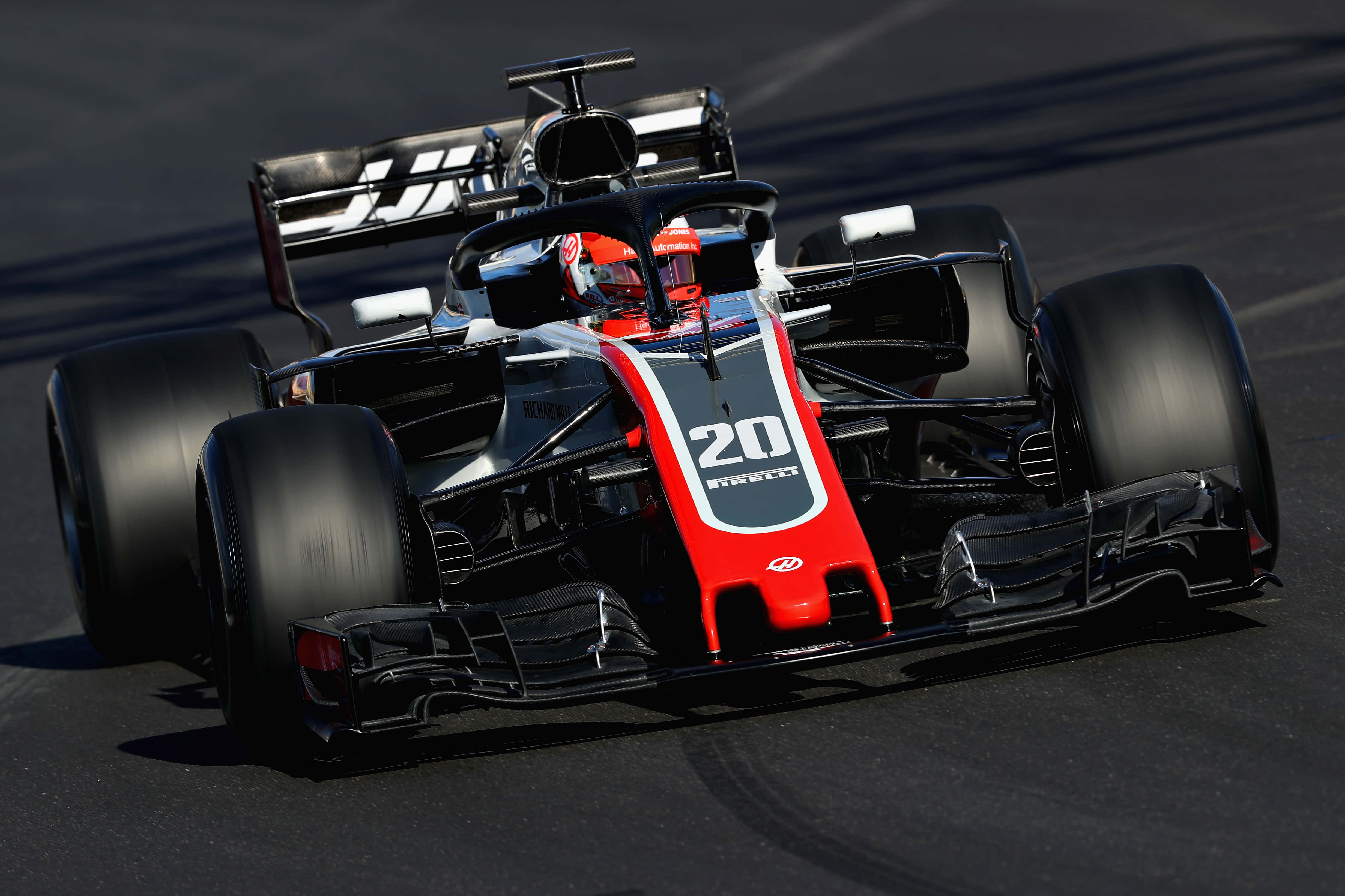 F1 桌布 壁紙 — 一輛時尚的紅黑配色一級方程式賽車，車號20，在陽光明媚的賽道上奔馳，輪胎緊抓瀝青路面。
