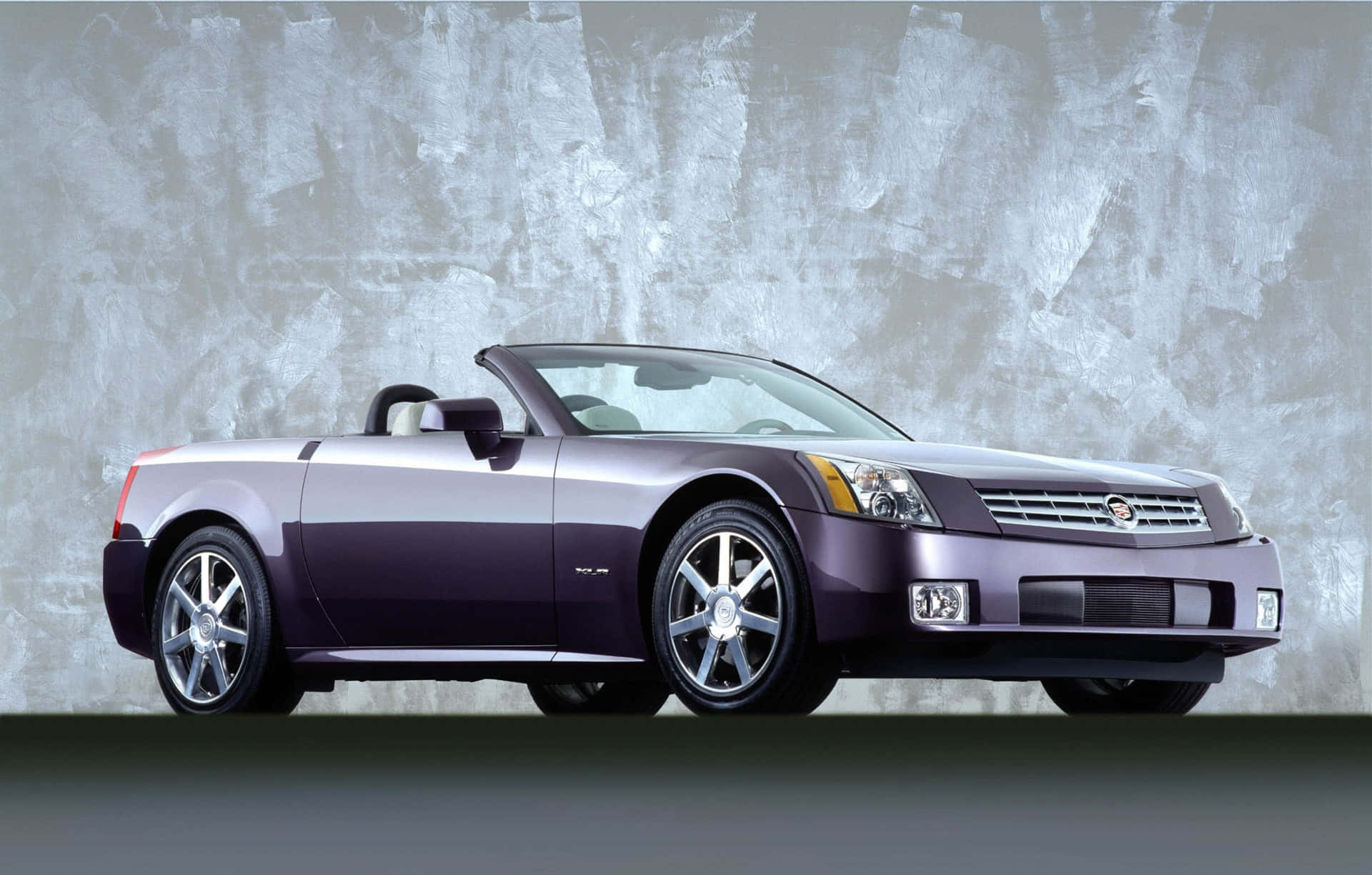 Cadillac Xlr 桌布 壁紙 — 一輛時尚的紫色敞篷跑車，帶有銀色裝飾，在質感灰色工作室背景中展示。