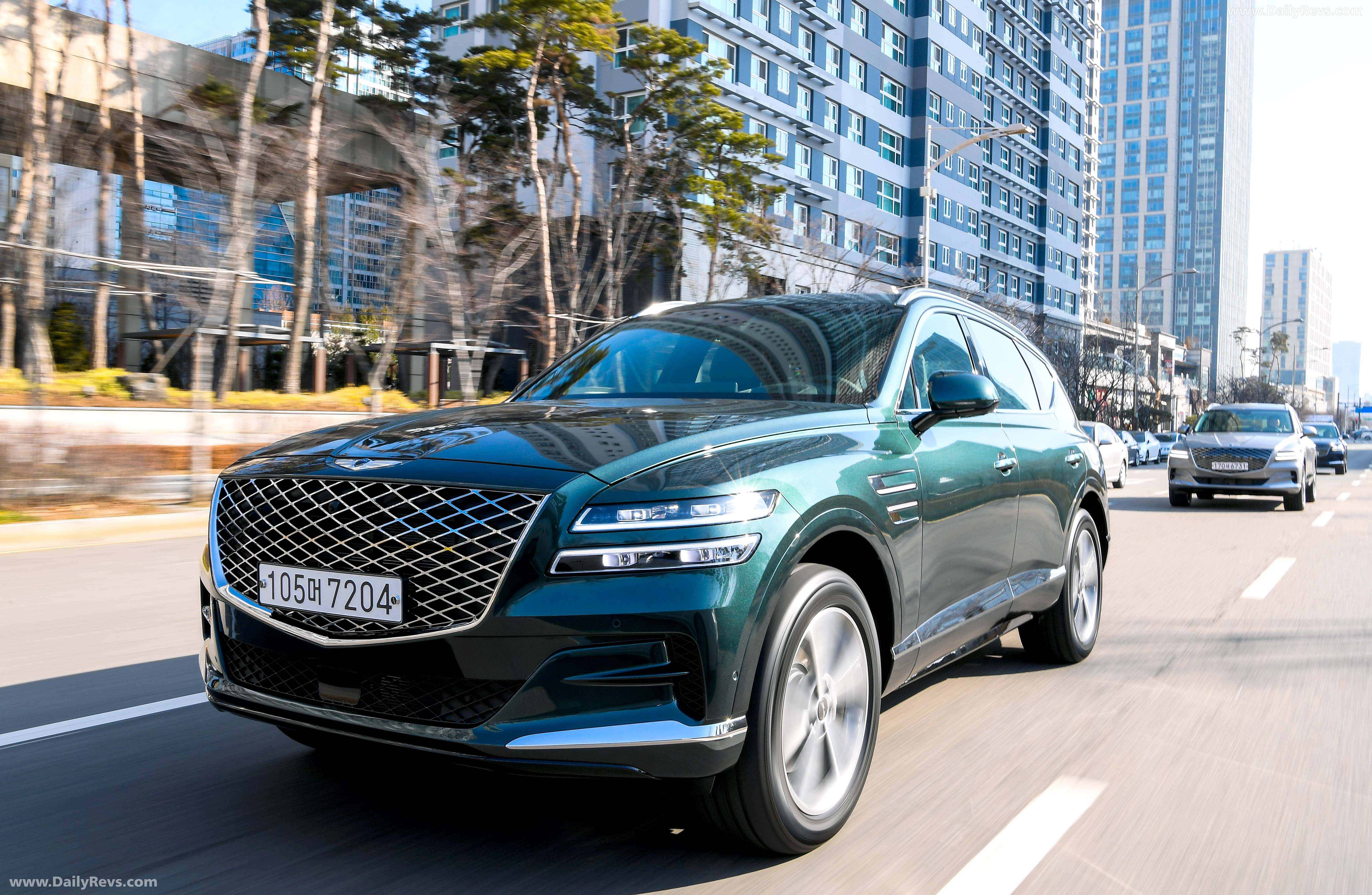 Genesis Gv80 桌布 壁紙 — 一輛時尚的綠色Genesis GV80 SUV行駛在陽光明媚的城市街道上，兩旁是現代玻璃建築和光禿的樹木。