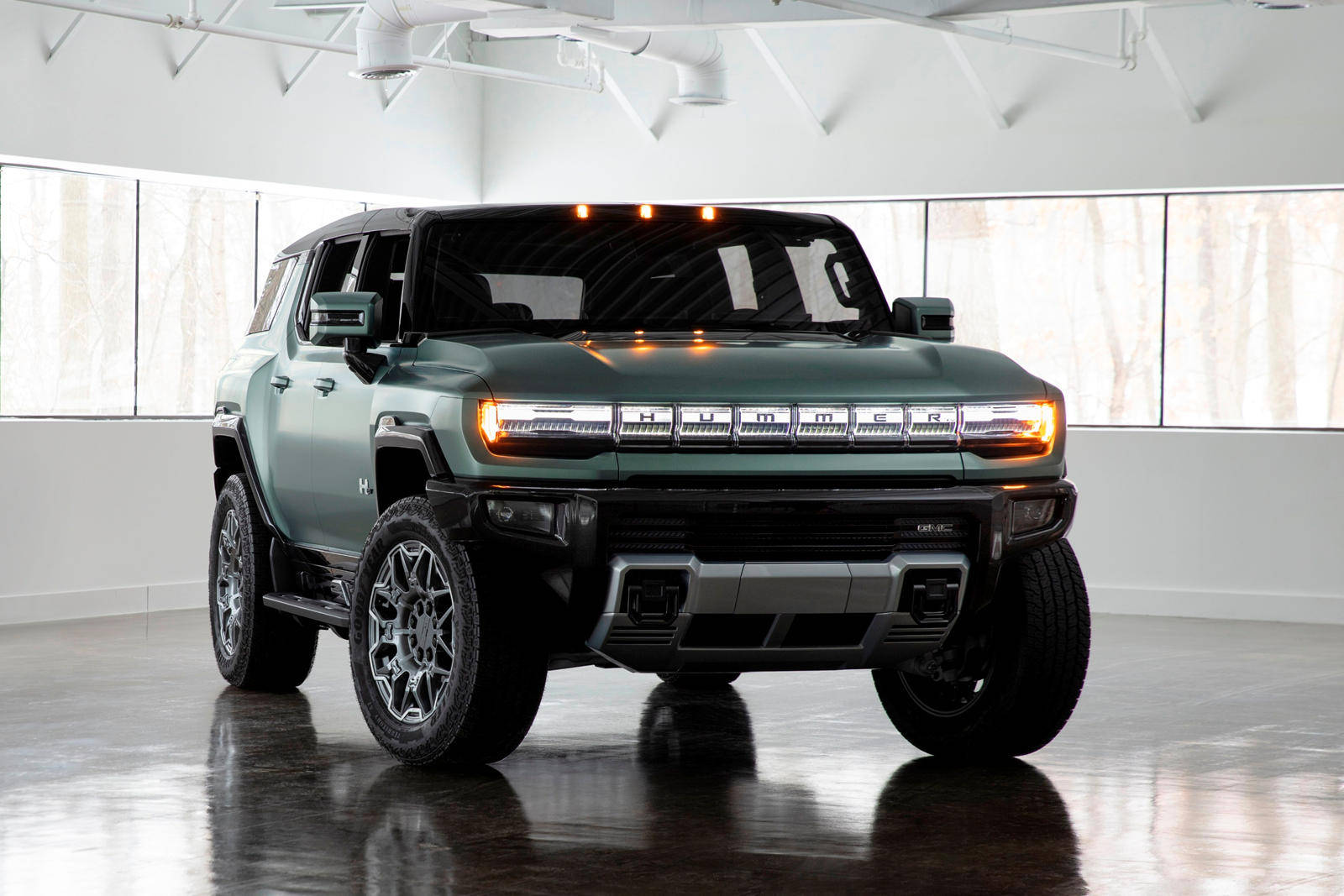 Truck 桌布 壁紙 — 一輛時尚的綠色Hummer EV SUV，配備發光頭燈，在簡約白色工作室中展示，地板具有反射效果。