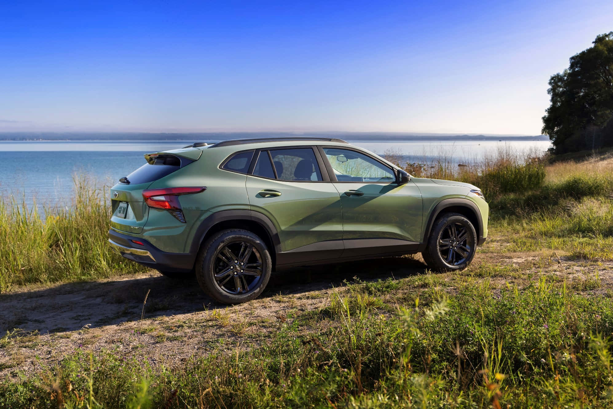Chevrolet 桌布 壁紙 — 一輛時尚的綠色SUV停泊在青草岸邊，旁邊是平靜的藍色湖泊，天空晴朗。