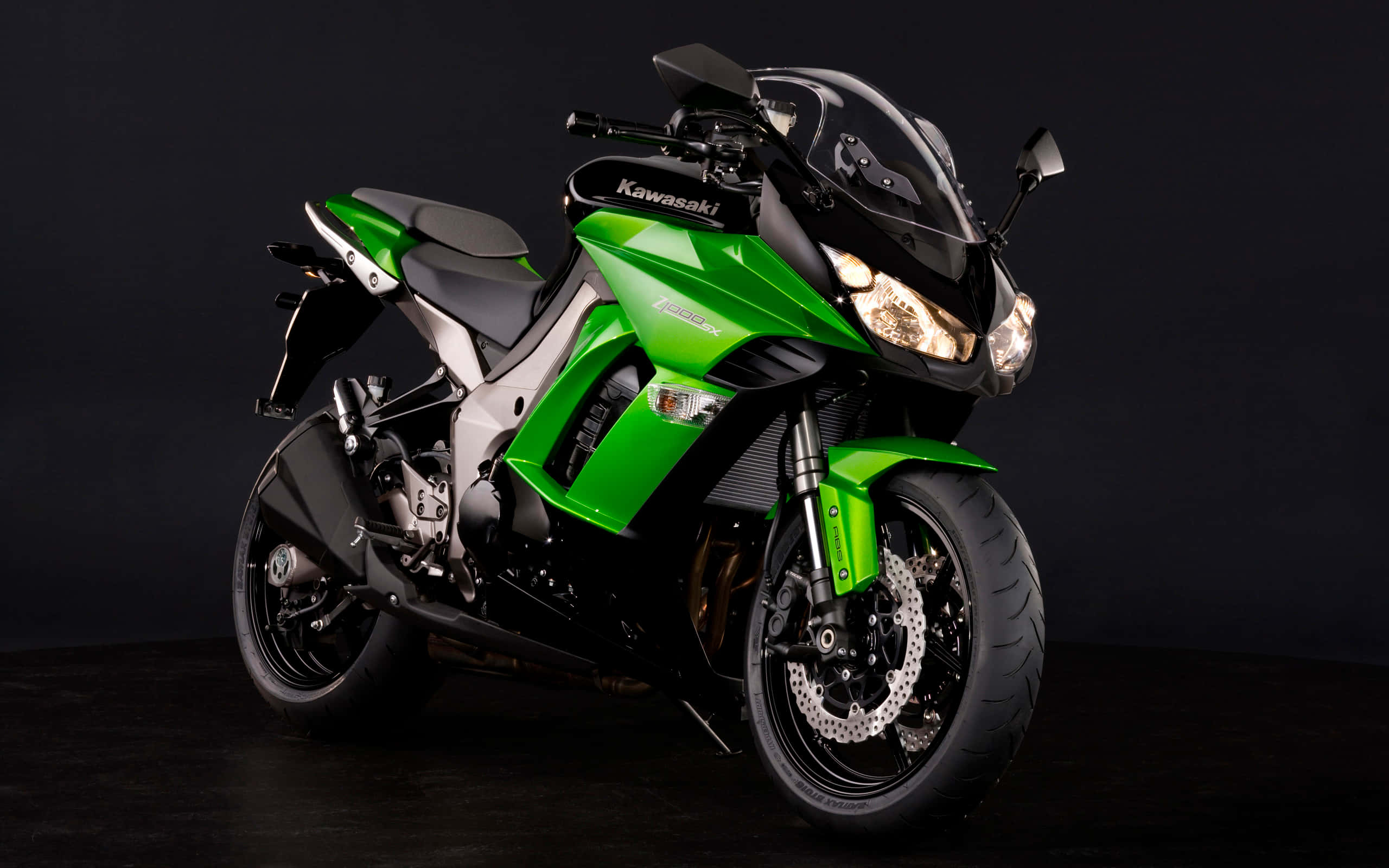 Kawasaki Desktop 桌布 壁紙 — 一輛時尚的綠色和黑色 Kawasaki 運動摩托車，配備發光頭燈，以深色工作室背景為襯托。