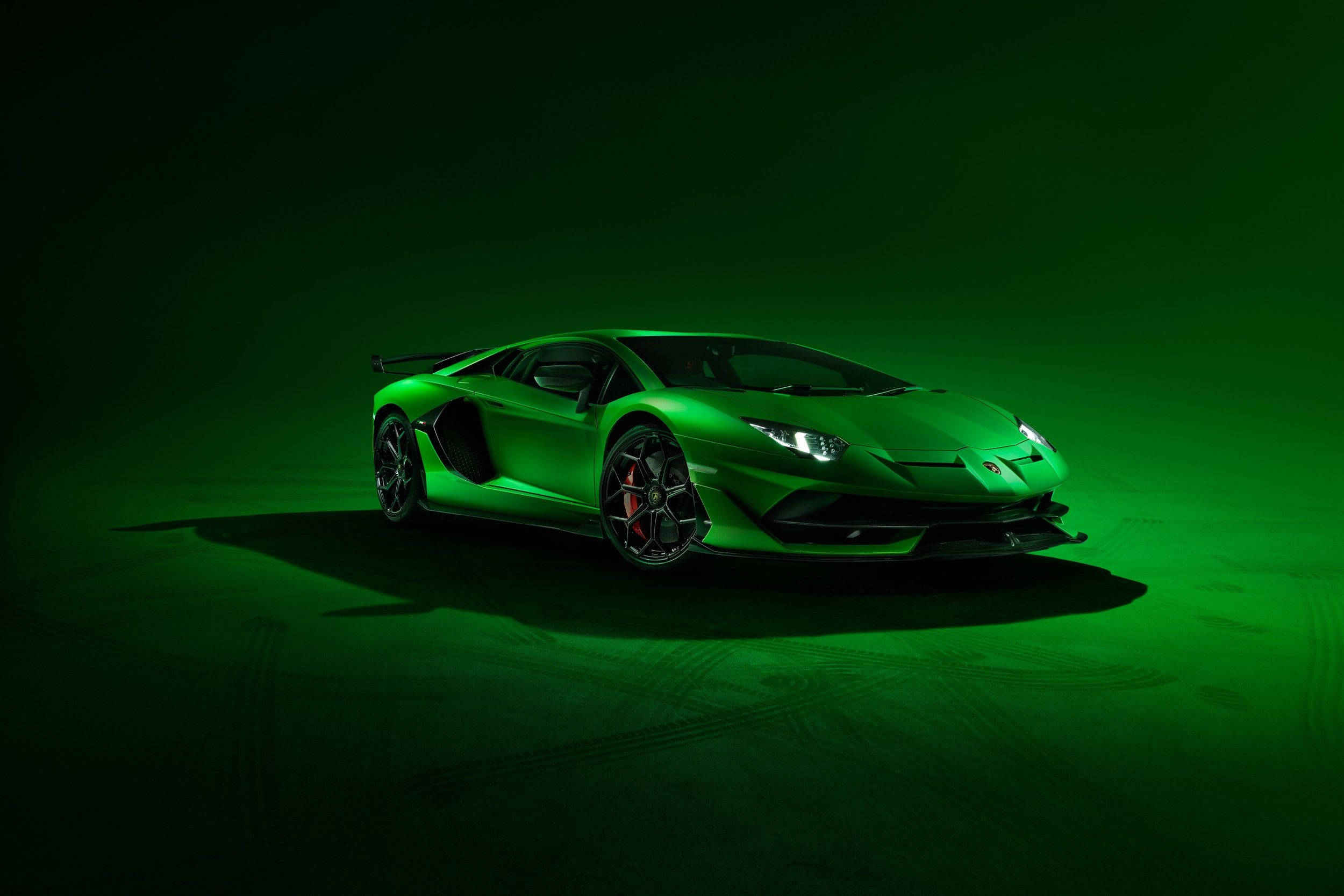 汽車 桌布 壁紙 — 一輛時尚的綠色藍寶堅尼 Aventador SVJ 在黑暗的攝影棚地板上，在戲劇性的綠色燈光下閃耀，地板上帶有輪胎痕跡。
