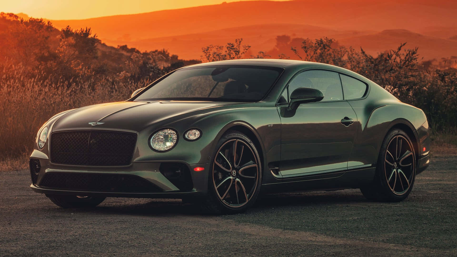 桌布 壁紙 — 一輛時尚的綠色賓利 Continental GT 雙門跑車停在日落時分的碎石路上，背景是綿延起伏的山丘。
