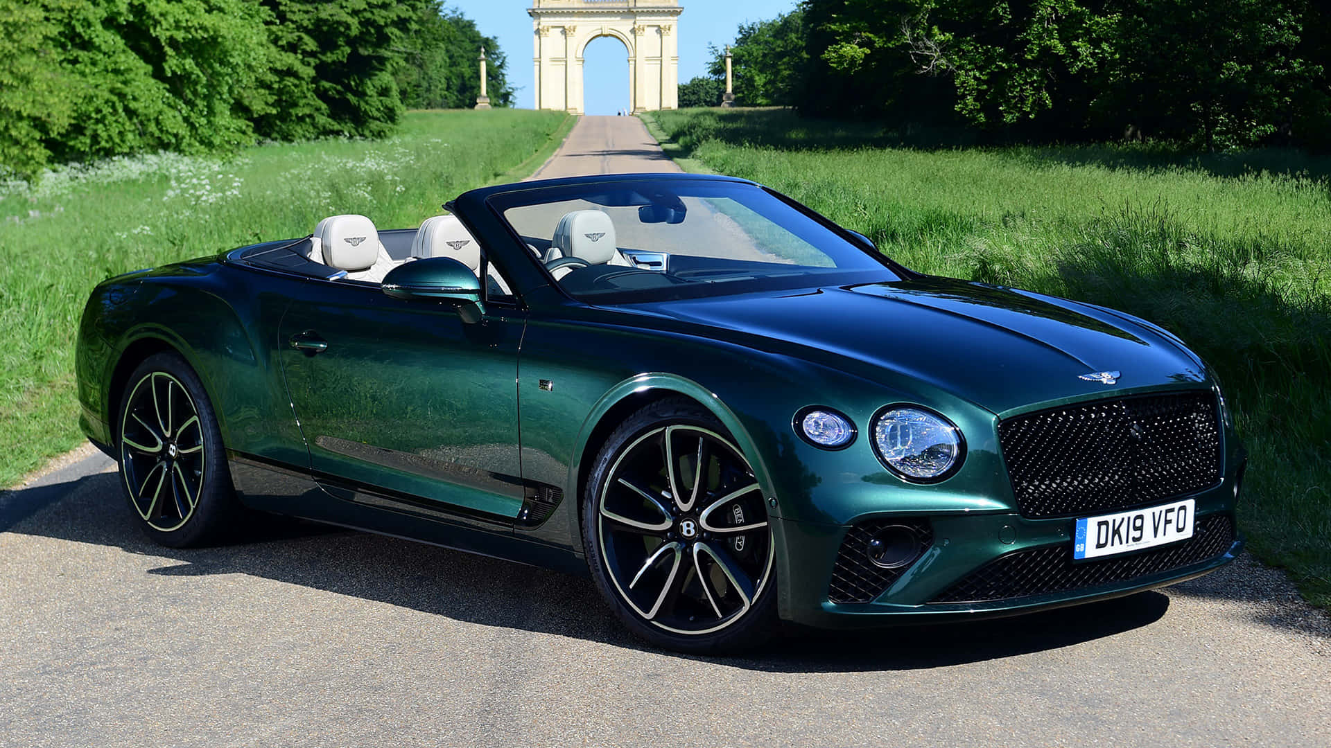 Bentley Continental Gt Convertible 桌布 壁紙 — 一輛時尚的綠色賓利敞篷車停在碎石路上，背景是一座宏偉的石拱門，在明亮的陽光下。
