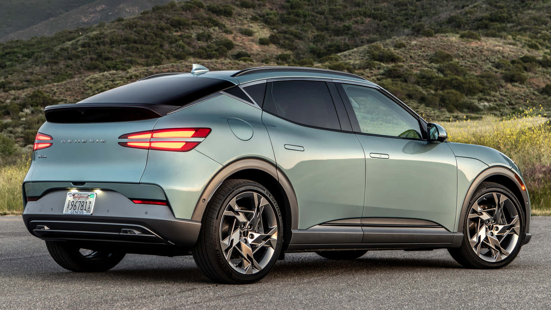 Genesis Gv60 桌布 壁紙 — 一輛時尚的薄荷綠色 Genesis GV60 電動 SUV 停在柏油路上，背景是山丘和野花。
