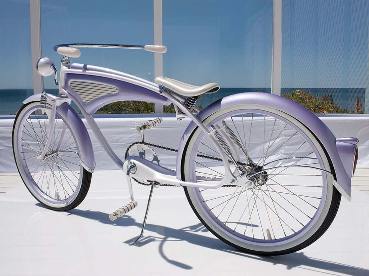 Beach Cruiser 桌布 壁紙 — 一輛時尚的薰衣草色自行車，帶有鍍鉻裝飾，矗立在白色平台上，背景是明亮的藍色海洋。