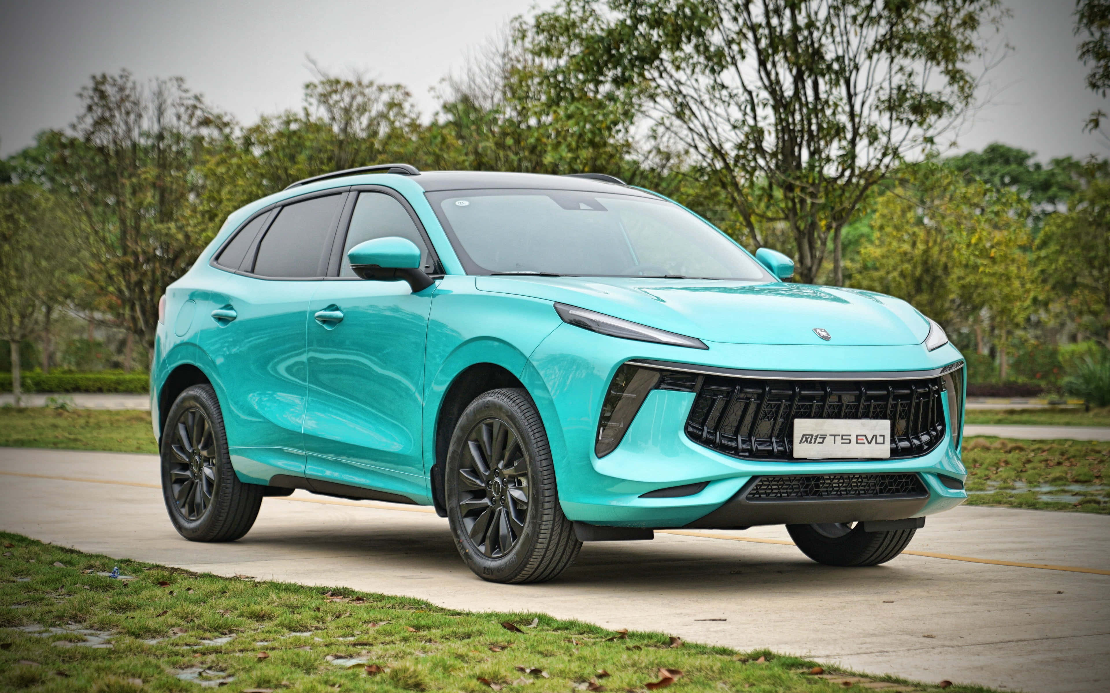 Dongfeng 桌布 壁紙 — 一輛時尚的藍綠色SUV，帶有黑色飾邊，停泊在鋪砌的小路上，旁邊有綠草和樹木，天空多雲。