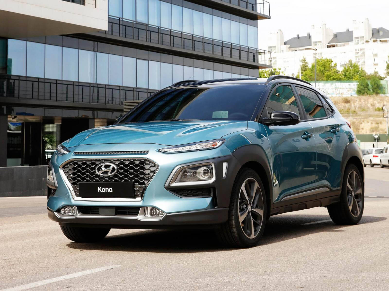Hyundai 桌布 壁紙 — 一輛時尚的藍綠色現代Kona SUV停放在現代玻璃建築前，陽光普照。