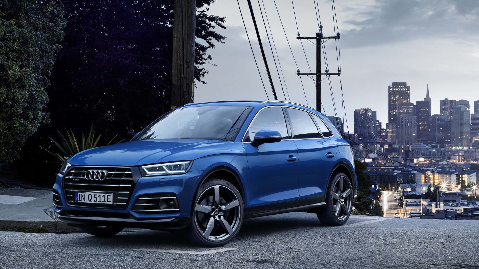 Audi Q5 桌布 壁紙 — 一輛時尚的藍色 Audi Q5 SUV 停泊在城市的山坡上，俯瞰著暮色中燈火通明的天際線。