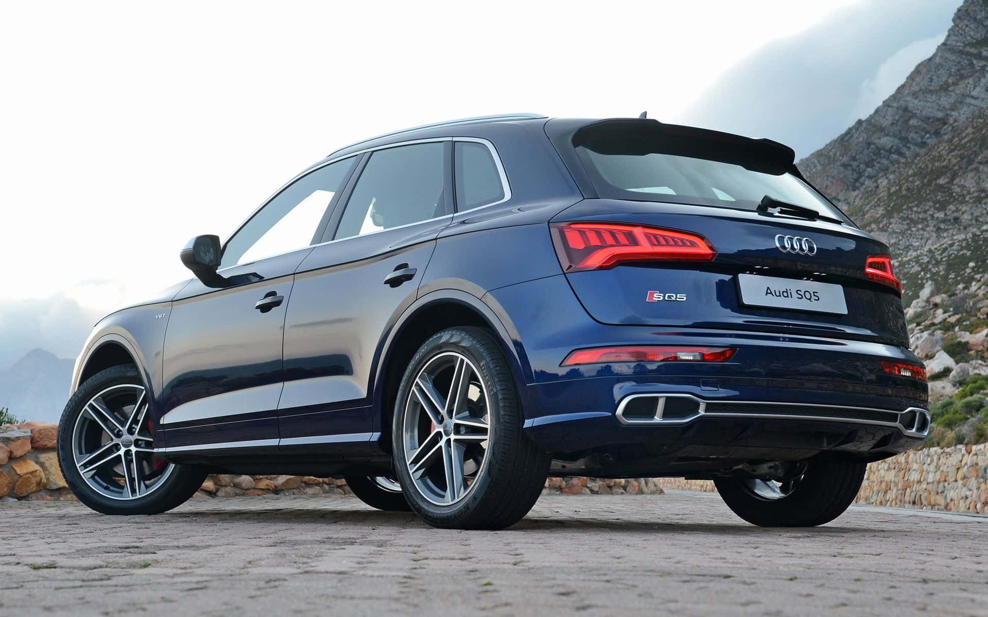 Audi Sq5 桌布 壁紙 — 一輛時尚的藍色 Audi SQ5 SUV 停泊在石徑上，背景是崎嶇的山脈，天空多雲。