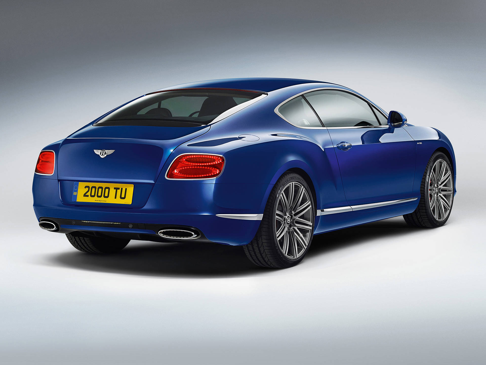 bentley HD 桌布 壁紙 — 一輛時尚的藍色 Bentley Continental GT 雙門轎跑車，從後方四分之三角度拍攝，背景為漸變灰色工作室背景。