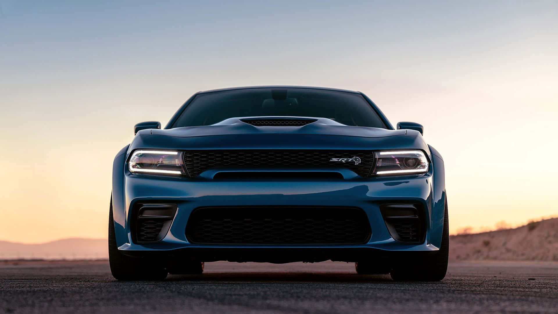 Dodge Charger 桌布 壁紙 — 一輛時尚的藍色 Dodge Challenger SRT Hellcat 在日落時分的沙漠公路上向前行駛，天空色調溫暖。