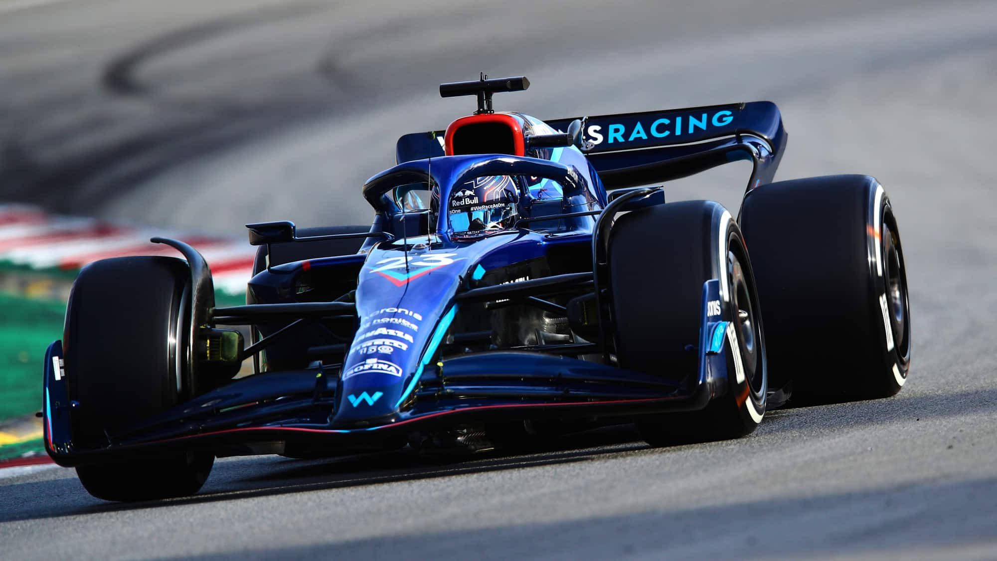 F1 桌布 壁紙 — 一輛時尚的藍色 Formula E 賽車在明亮的日光下，在設有紅色和白色路緣石的賽道上飛馳。