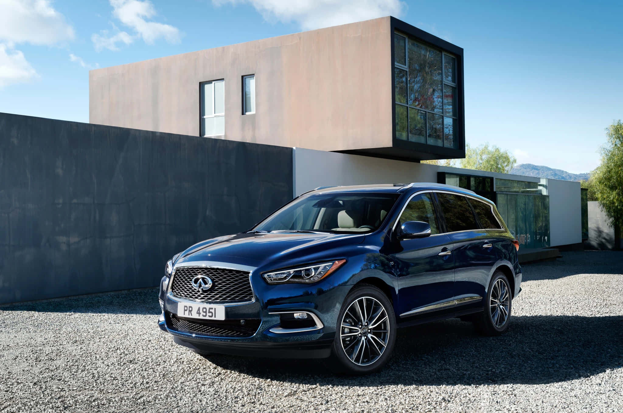 Infiniti Qx60 桌布 壁紙 — 一輛時尚的藍色 Infiniti QX60 SUV 停泊在碎石路上，前方是一座現代簡約風格的房屋，背景是清澈的藍天。