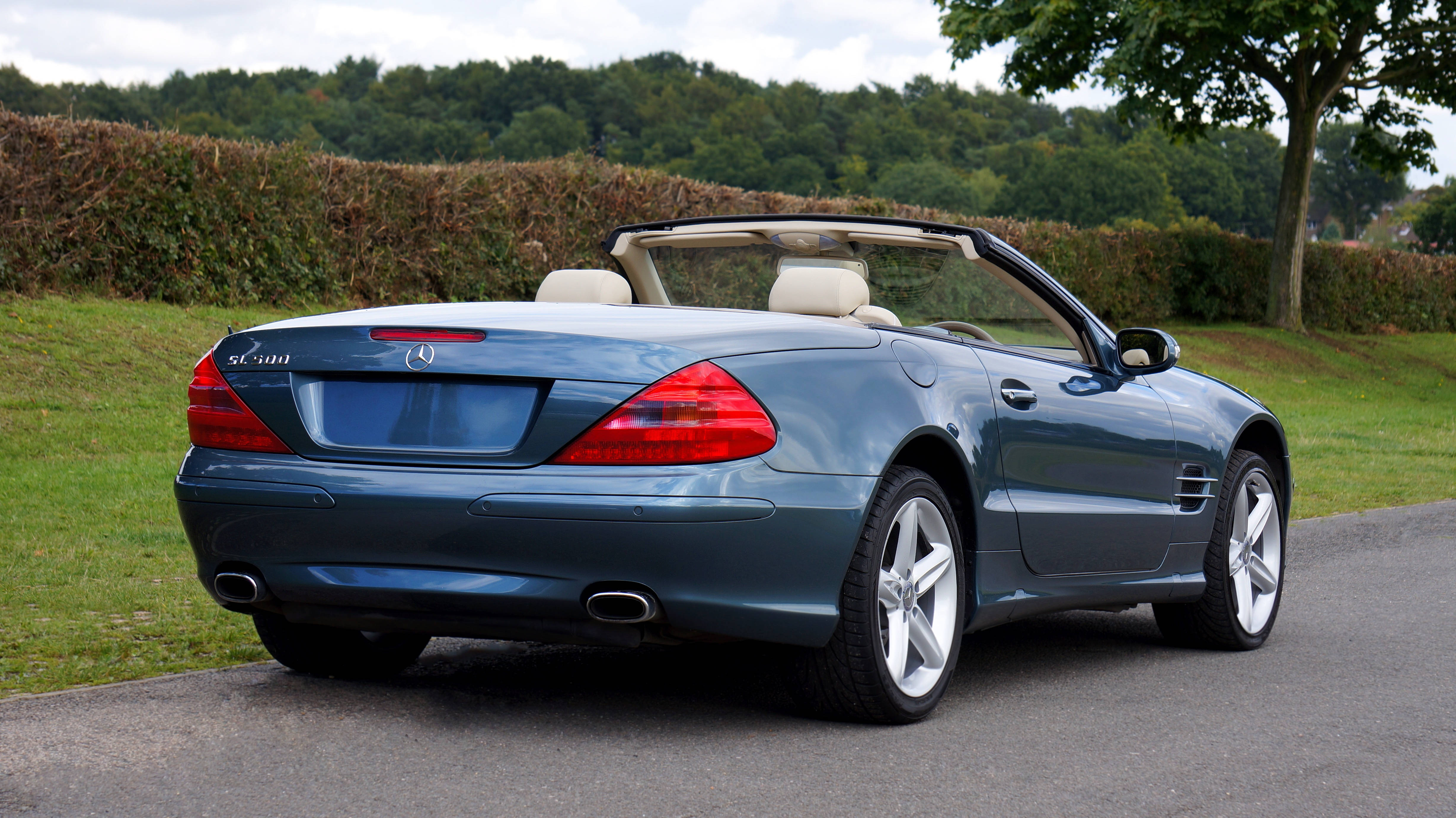 benz 4K 桌布 壁紙 — 一輛時尚的藍色 Mercedes SL500 敞篷車停在鋪砌的道路上，背景有綠草和樹木。