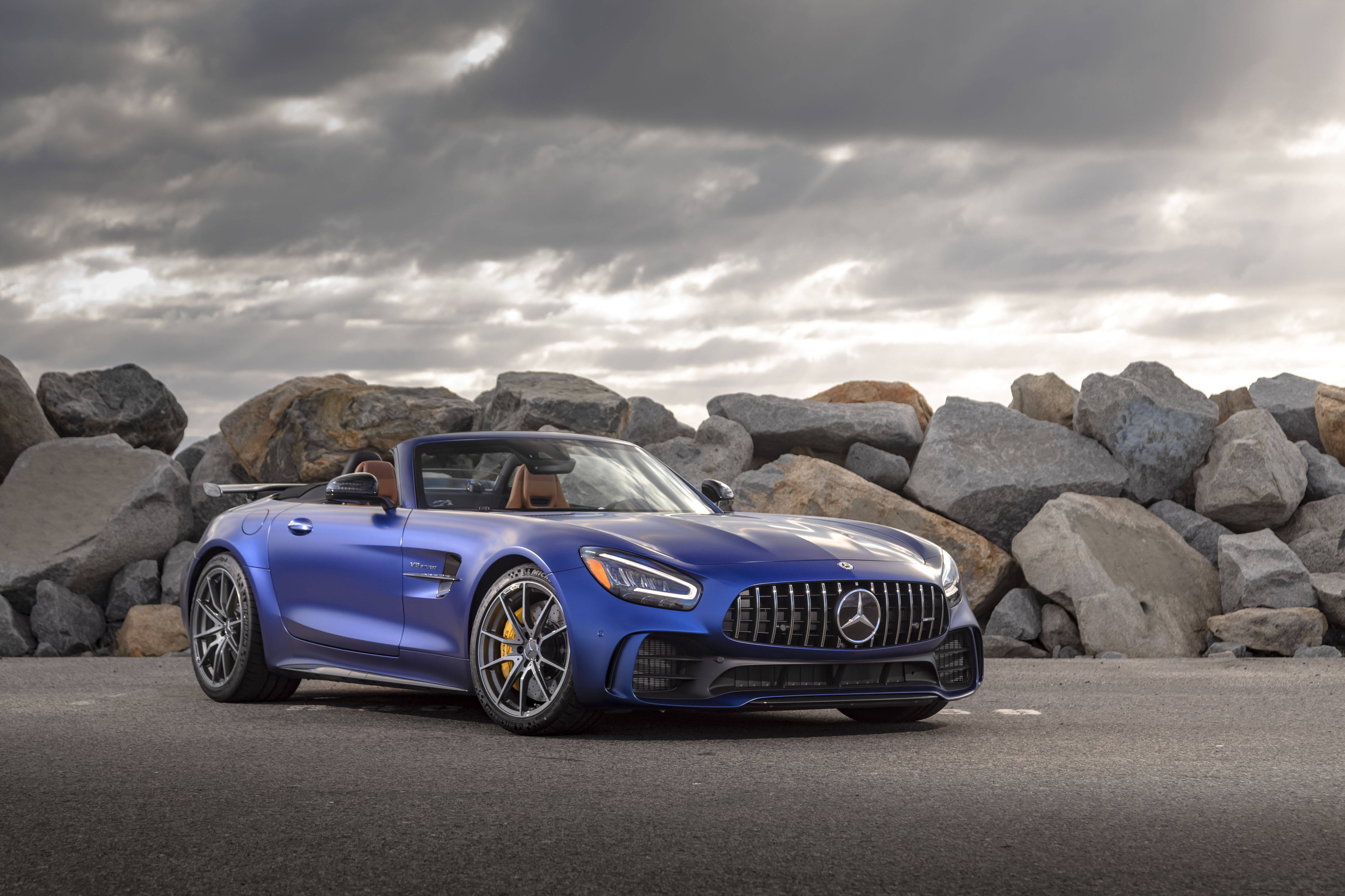 Gtr 桌布 壁紙 — 一輛時尚的藍色 Mercedes-AMG GT R 敞篷跑車停泊在瀝青路上，旁邊有巨石，天空戲劇性地多雲。