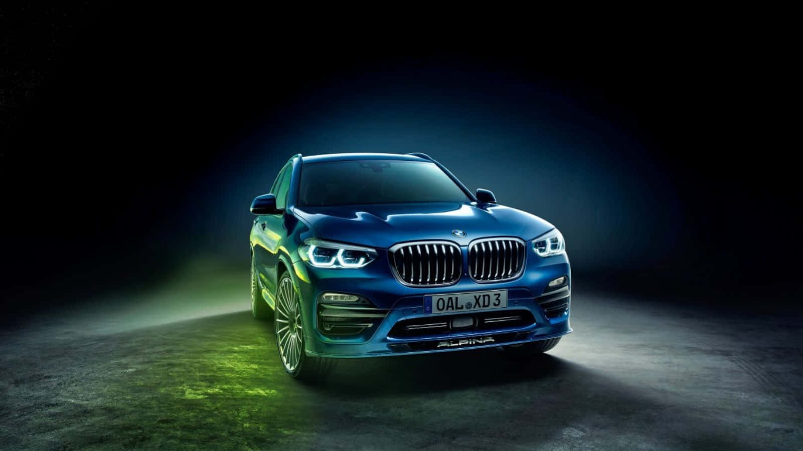 Bmw Tablet 桌布 壁紙 — 一輛時尚的藍色Alpina BMW SUV在戲劇性的攝影棚燈光下發光，綠色地板反射在黑暗背景上。