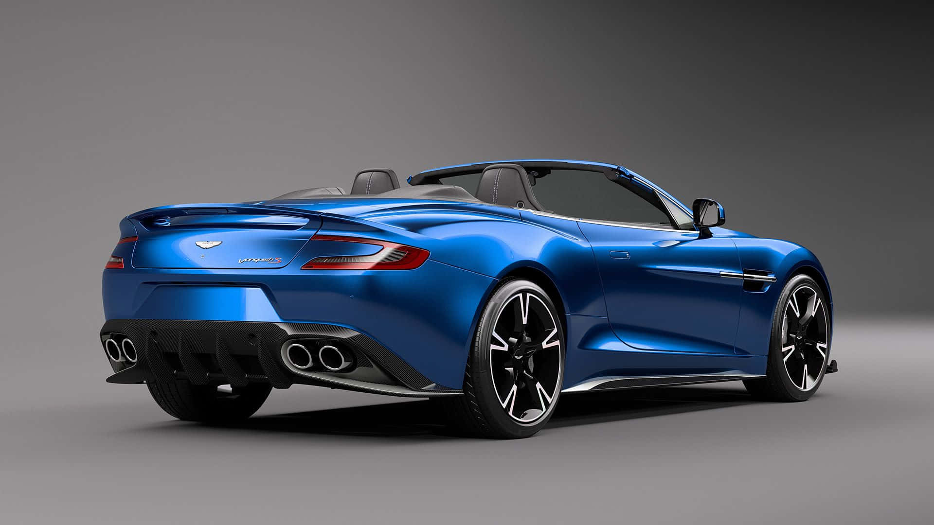 Aston Martin Vanquish 桌布 壁紙 — 一輛時尚的藍色Aston Martin V12 Vantage敞篷車，從後方四分之三角度展示，配備黑色輪圈和四出排氣管，背景為灰色攝影棚。