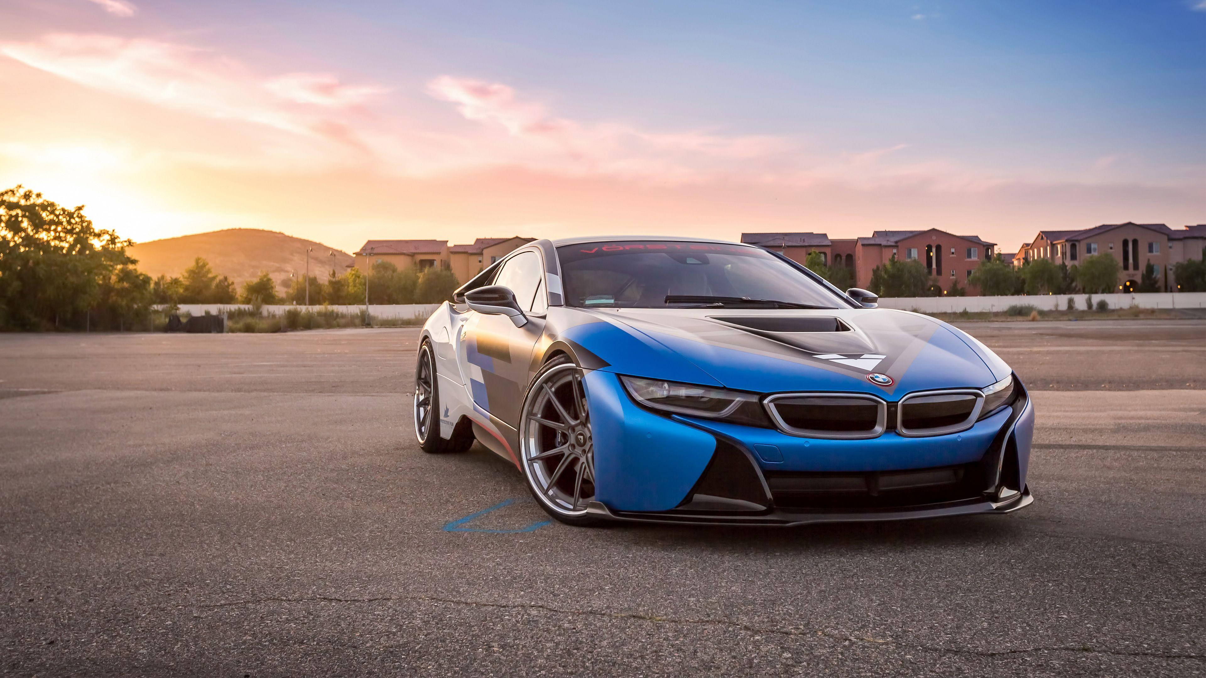 4K BMW 壁紙 桌布 壁紙 — 一輛時尚的藍色BMW i8跑車停在夕陽下的瀝青路上，背景是溫暖的天空和遠處的房屋。
