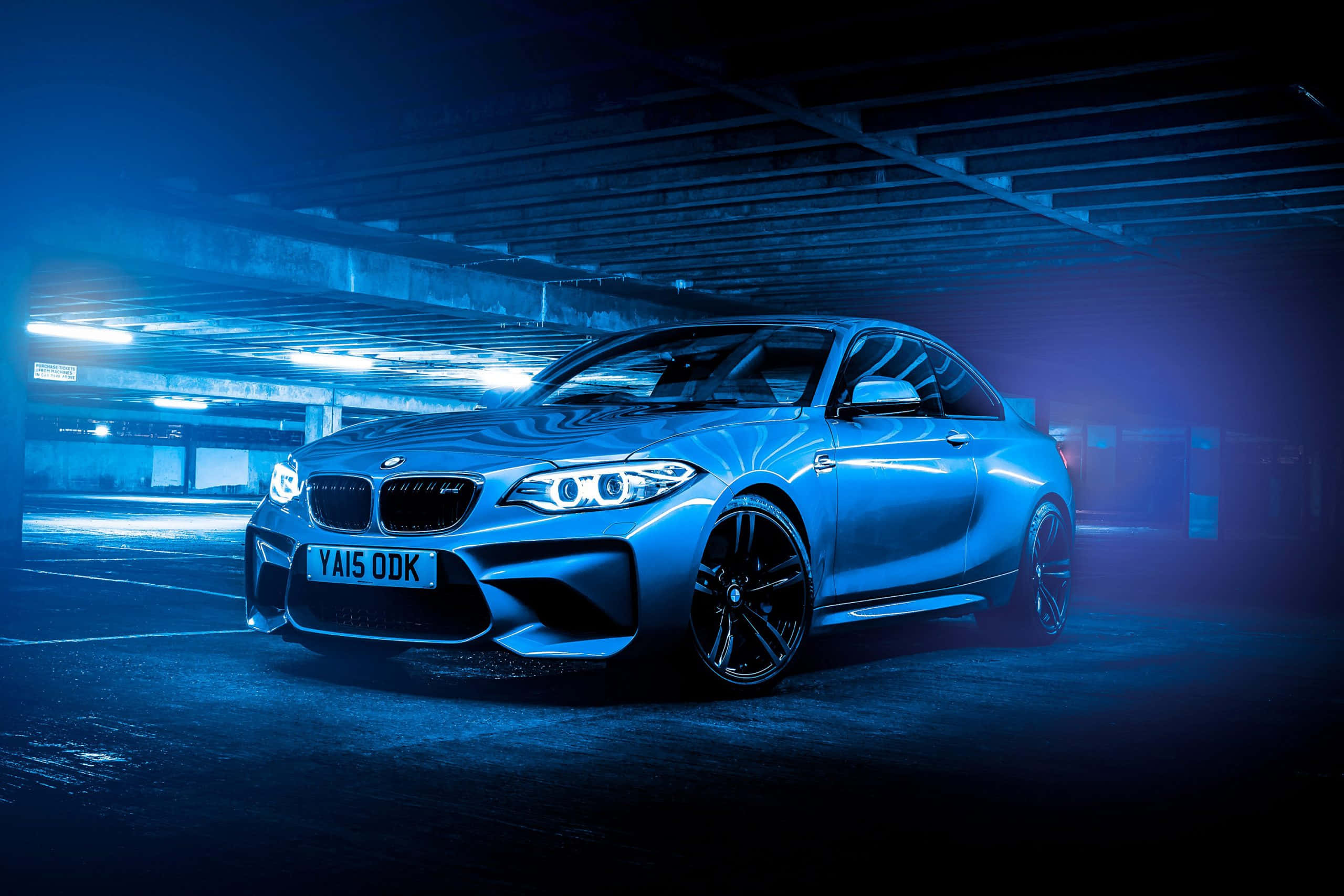 BMW 動圖 桌布 壁紙 — 一輛時尚的藍色BMW M2轎跑車在昏暗的地下停車場中，在霓虹燈下閃閃發光。