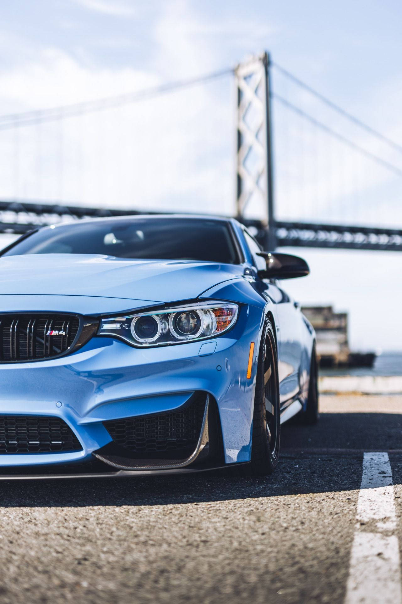 X 桌布 壁紙 — 一輛時尚的藍色BMW M4跑車停泊在道路上，背景是晴朗天空下的海灣大橋。