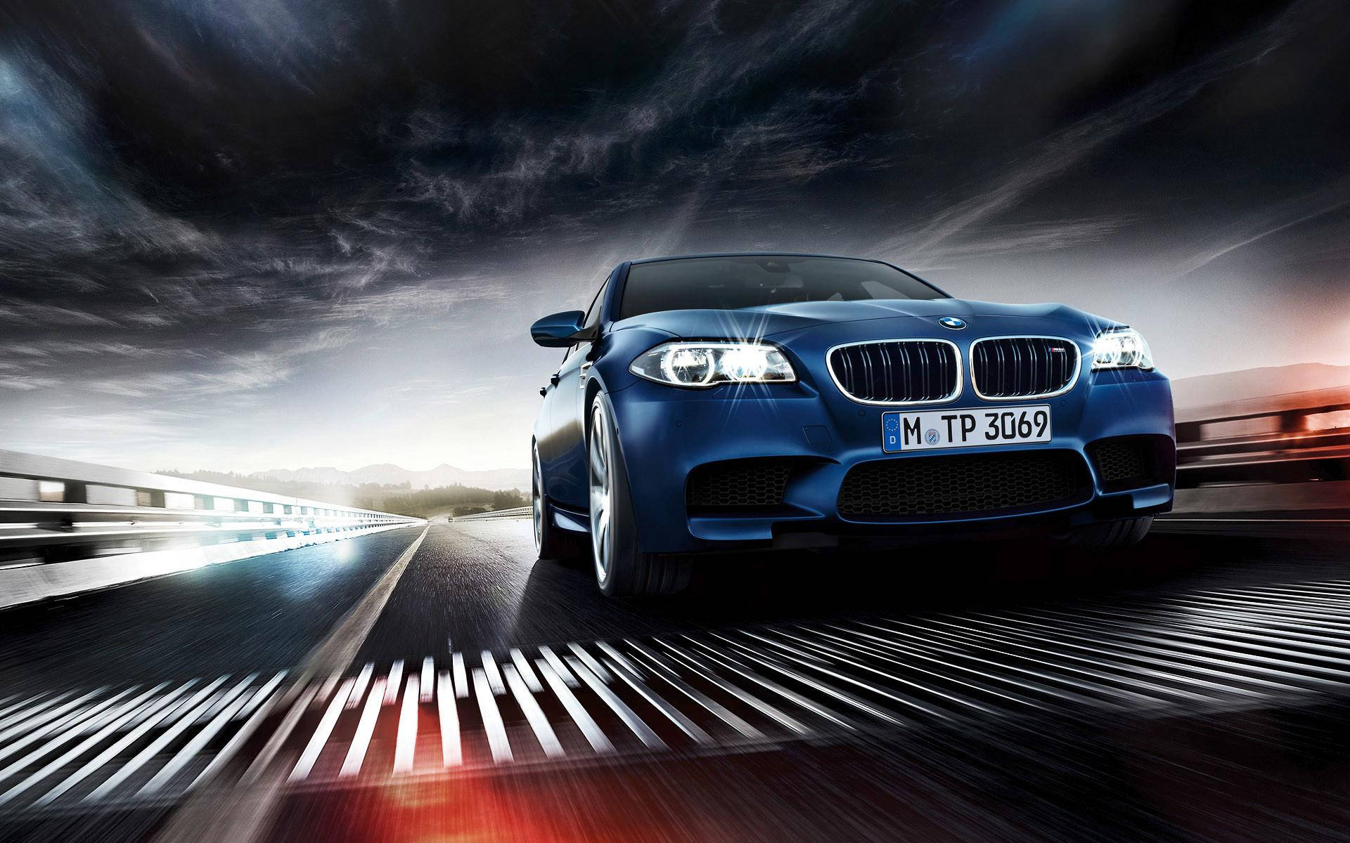 BMW 動圖 桌布 壁紙 — 一輛時尚的藍色BMW M5在戲劇性的暴風雨天空下，以動態模糊效果在潮濕的高速公路上飛馳。