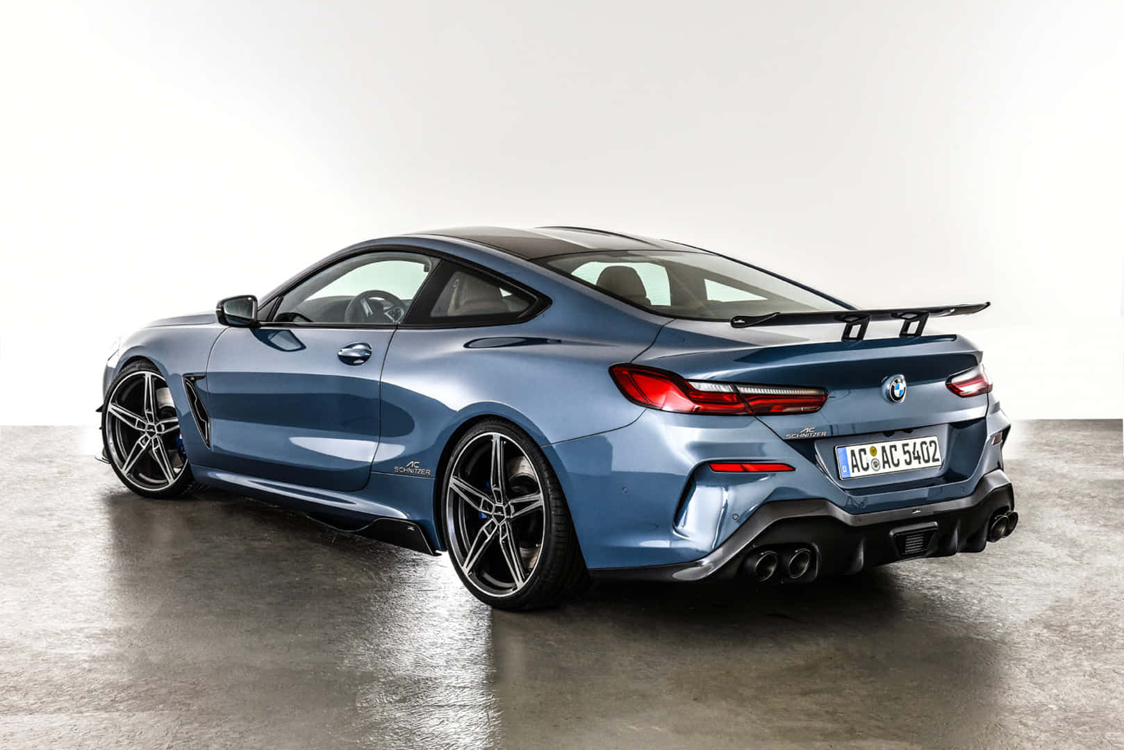 Bmw 8 Series 桌布 壁紙 — 一輛時尚的藍色BMW M8 Coupe，帶有黑色飾件和後擾流板，在極簡主義工作室中，拋光混凝土地板上靜立。