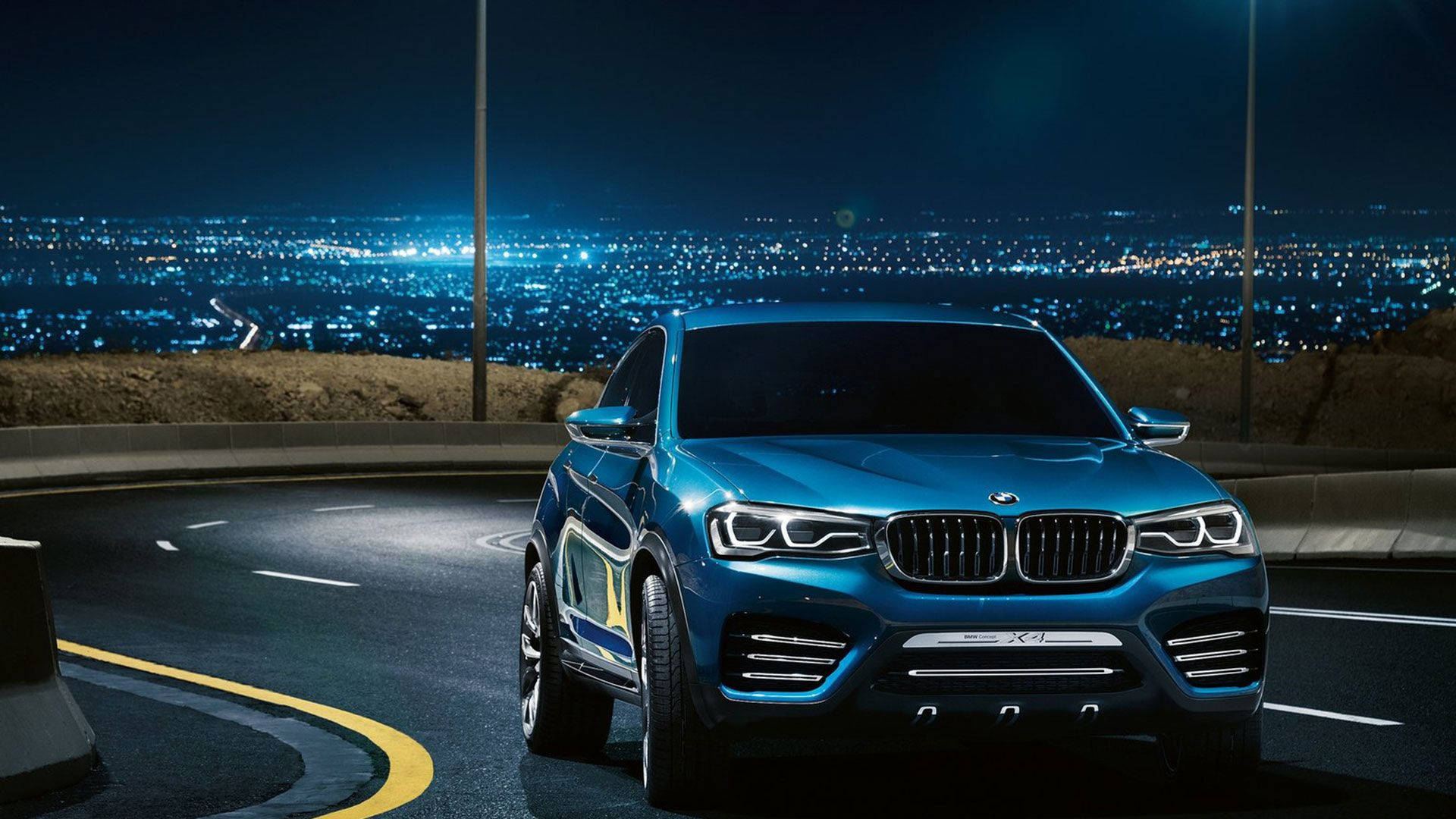 Luxury 桌布 壁紙 — 一輛時尚的藍色BMW SUV在夜間沿著蜿蜒的山路行駛，下方是閃爍的城市景觀。