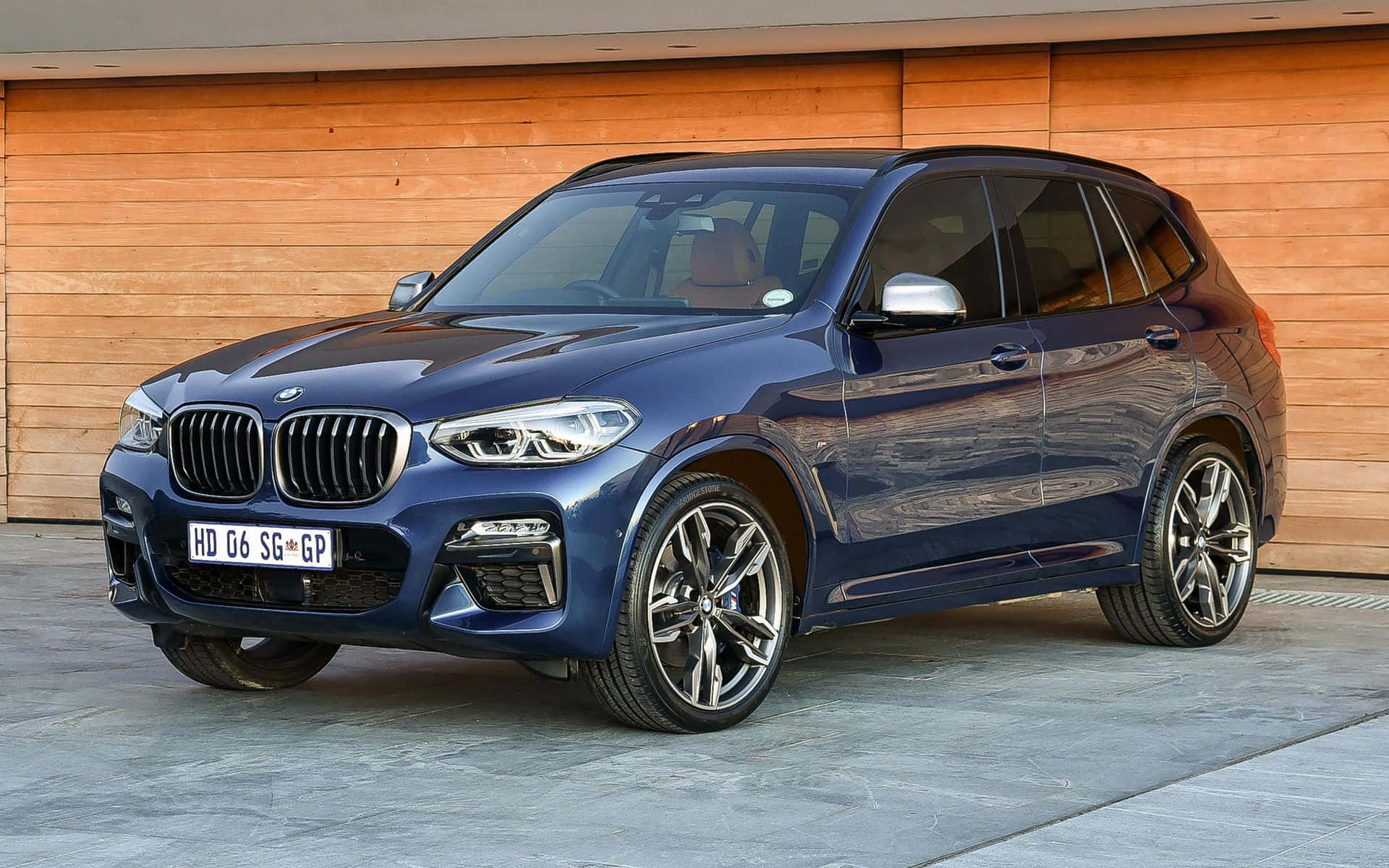 Bmw X3 桌布 壁紙 — 一輛時尚的藍色BMW X3 SUV停放在溫暖的木車庫前，拋光合金輪圈反射著環境光。