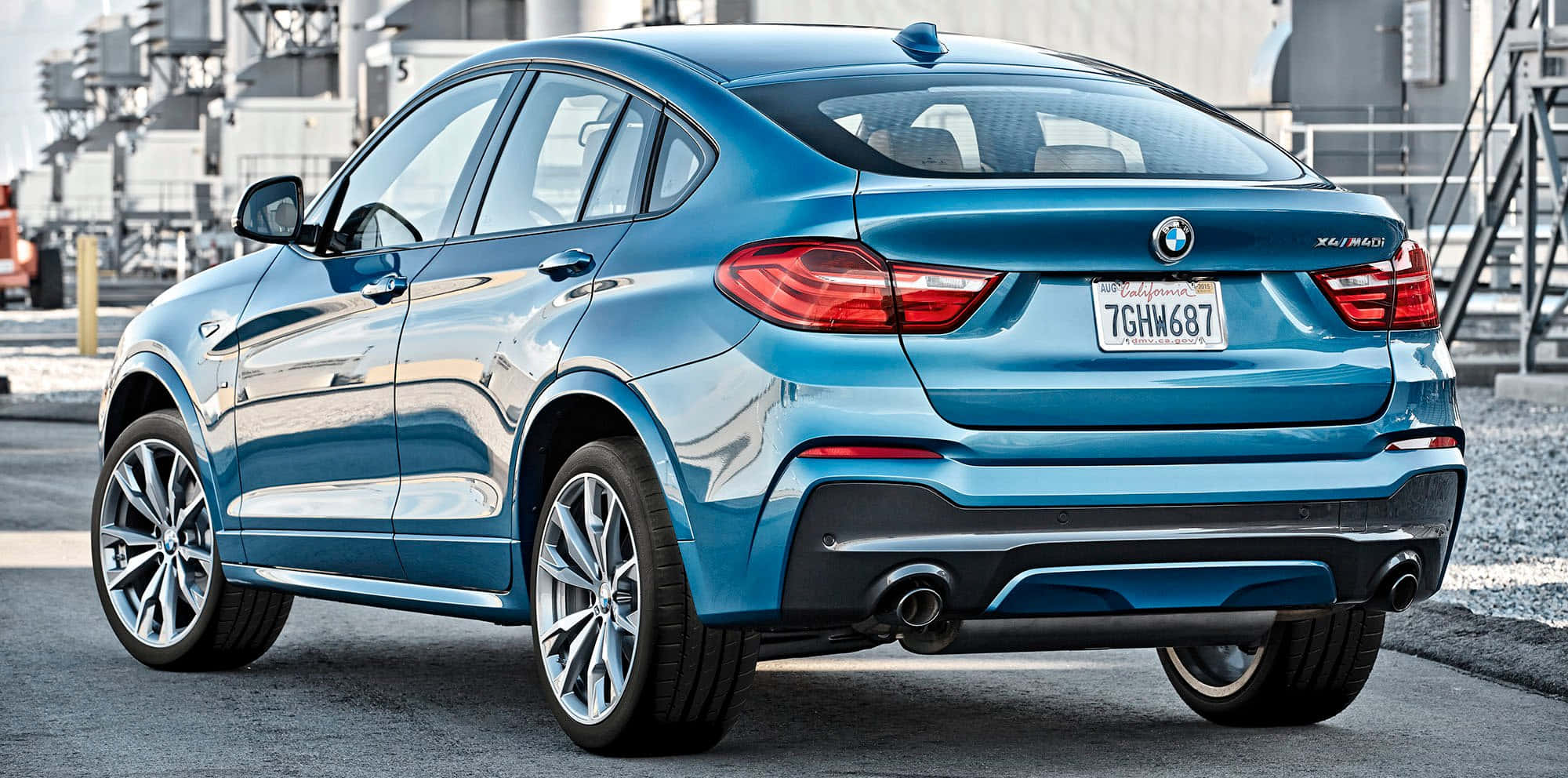 Bmw X4 桌布 壁紙 — 一輛時尚的藍色BMW X4 M40i SUV停放在柏油路上，背景是工業建築物。