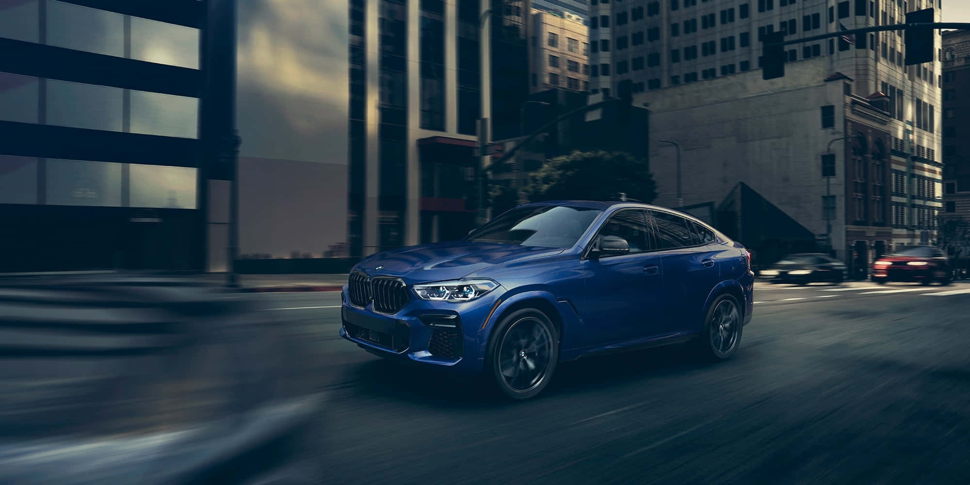 BMW X6 M 桌布 壁紙 — 一輛時尚的藍色BMW X6 Coupe在街道上飛馳，背景有高樓大廈和動態模糊效果。