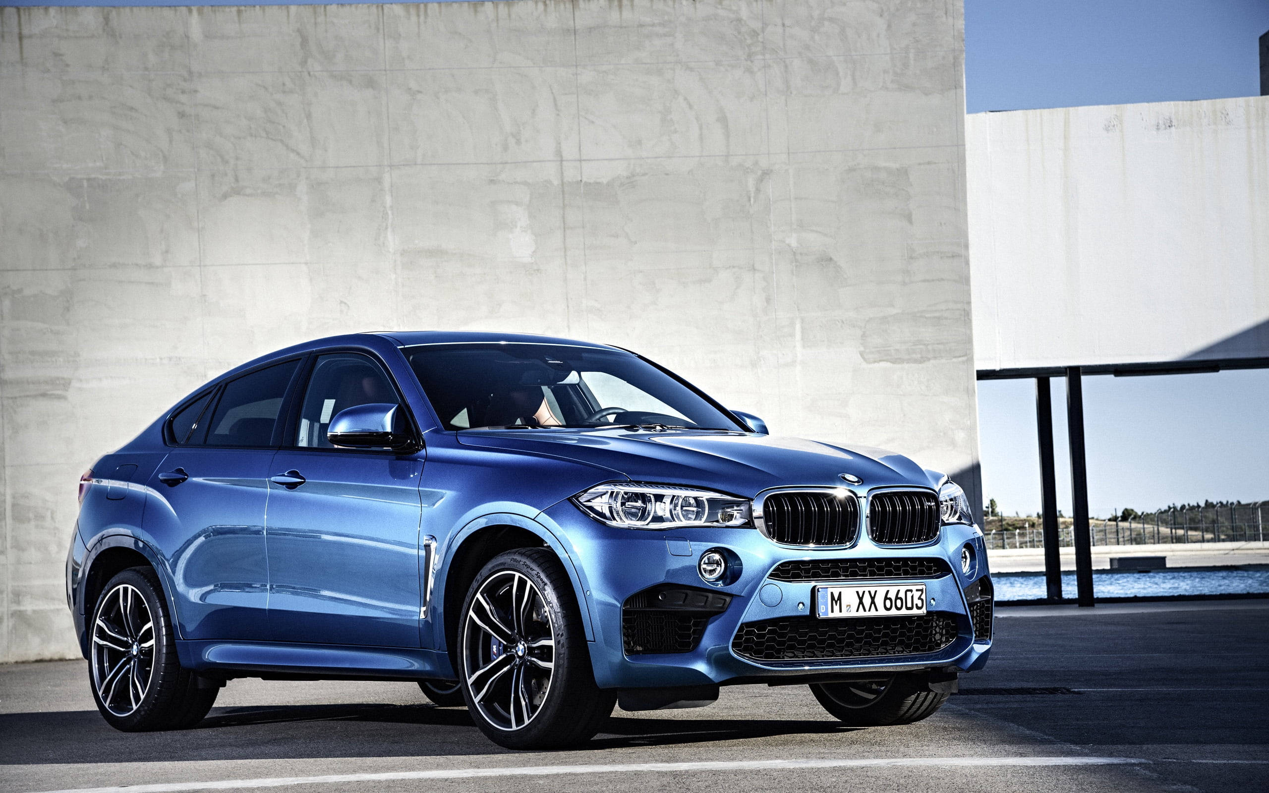 m 桌布 壁紙 — 一輛時尚的藍色BMW X6 M停放在極簡水泥牆旁，沐浴在明亮的日光下。