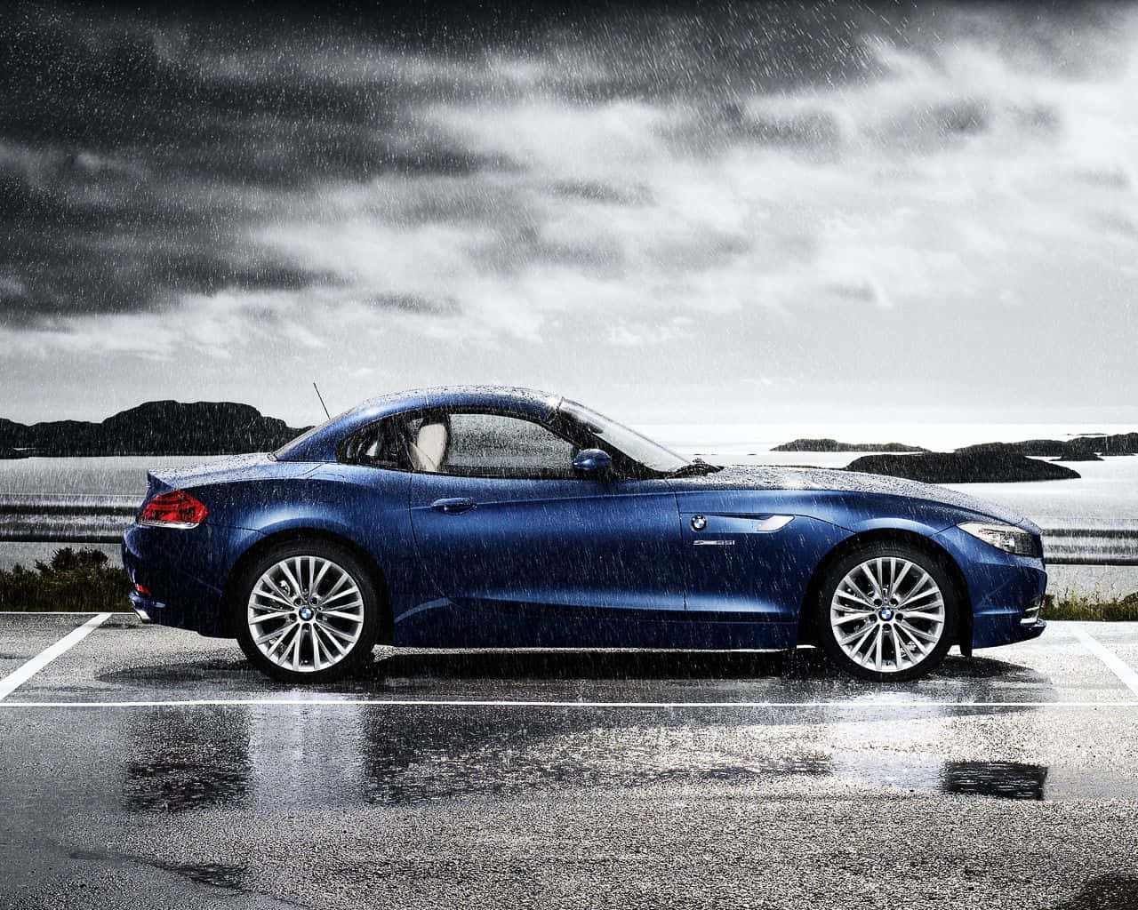 Bmw Z4 桌布 壁紙 — 一輛時尚的藍色BMW Z4敞篷車停在濕滑的停車場，上方是戲劇性的暴風雲。