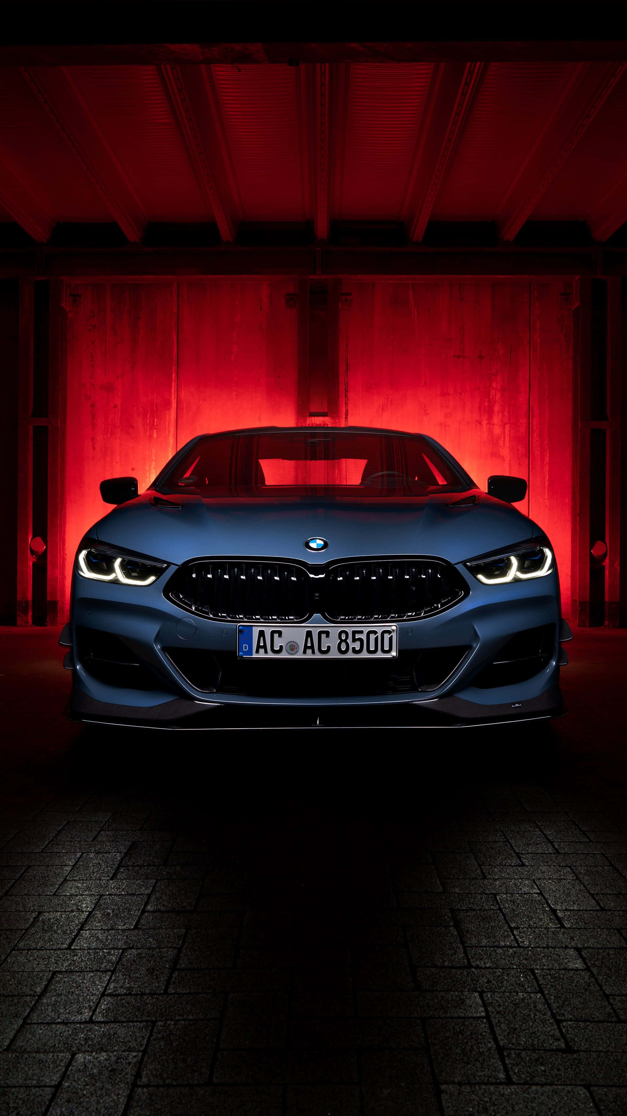 BMW 動圖 桌布 壁紙 — 一輛時尚的藍色BMW跑車在黑暗的工業車庫中，在戲劇性的紅色燈光下閃耀。