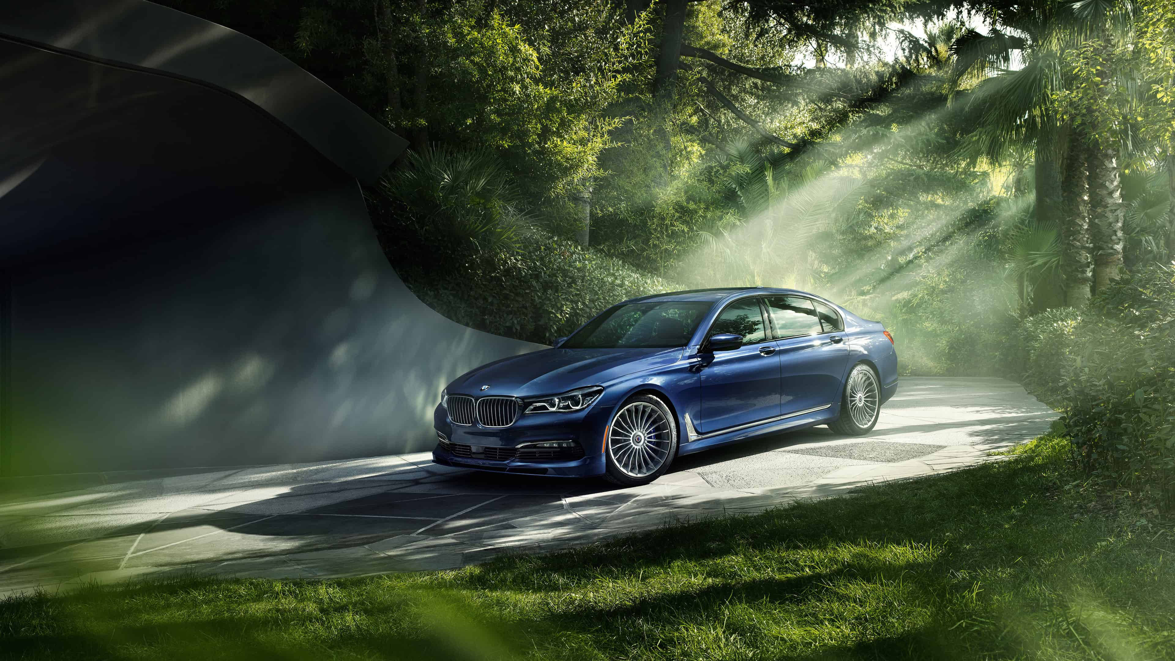 4K BMW 壁紙 桌布 壁紙 — 一輛時尚的藍色BMW轎車沿著一條霧氣瀰漫的森林道路行駛，沐浴在透過茂密綠樹灑落的金色陽光中。