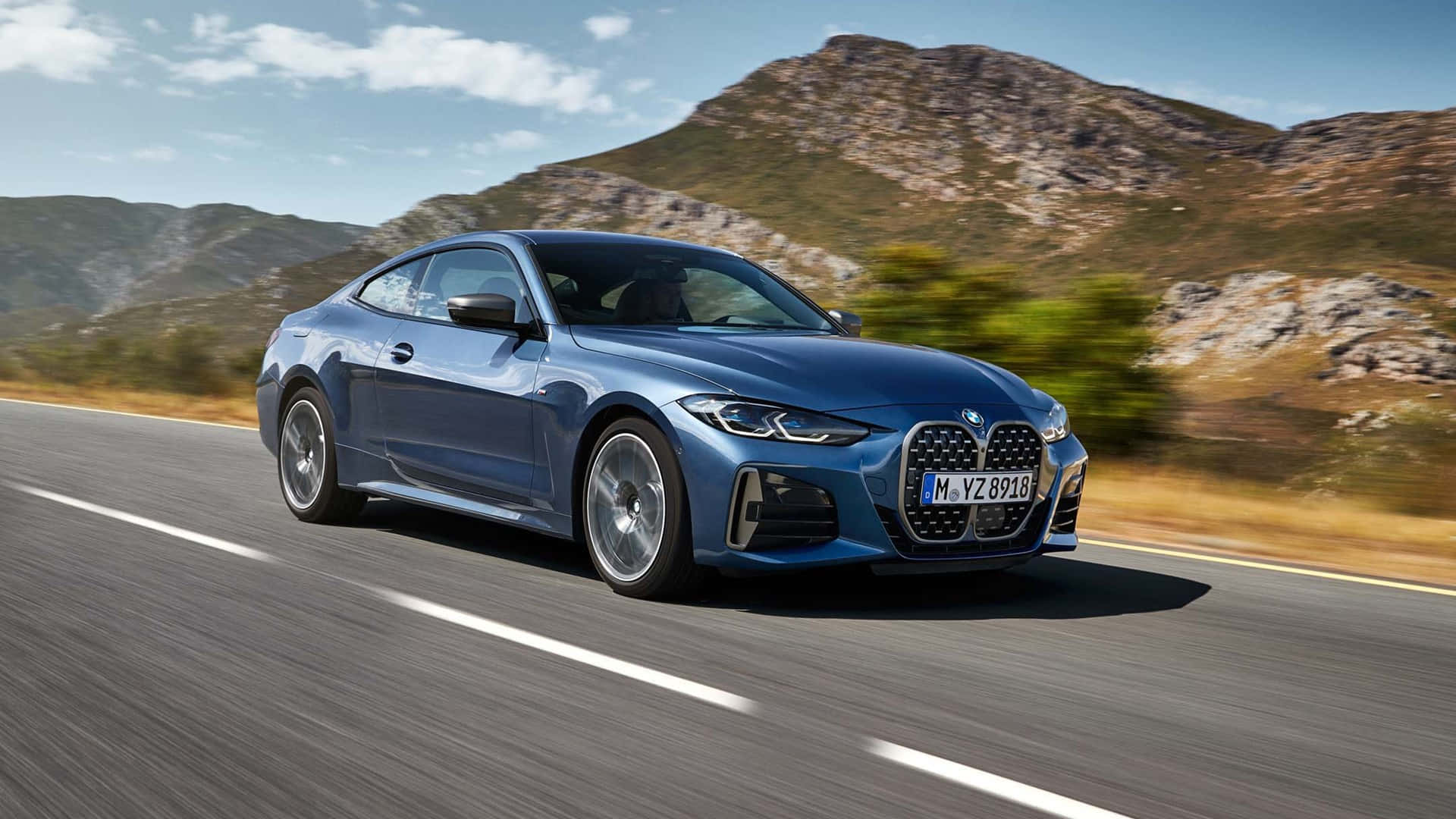 BMW 動圖 桌布 壁紙 — 一輛時尚的藍色BMW雙門跑車在晴朗的天空下沿著蜿蜒的山路飛馳。