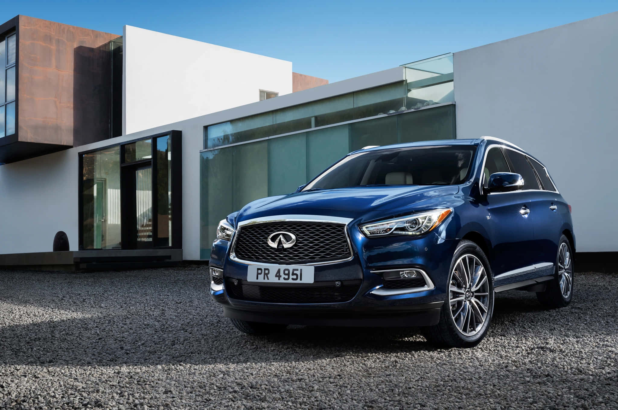 Infiniti Qx60 桌布 壁紙 — 一輛時尚的藍色Infiniti SUV停泊在碎石路上，前方是現代玻璃與混凝土房屋，天空清澈湛藍。