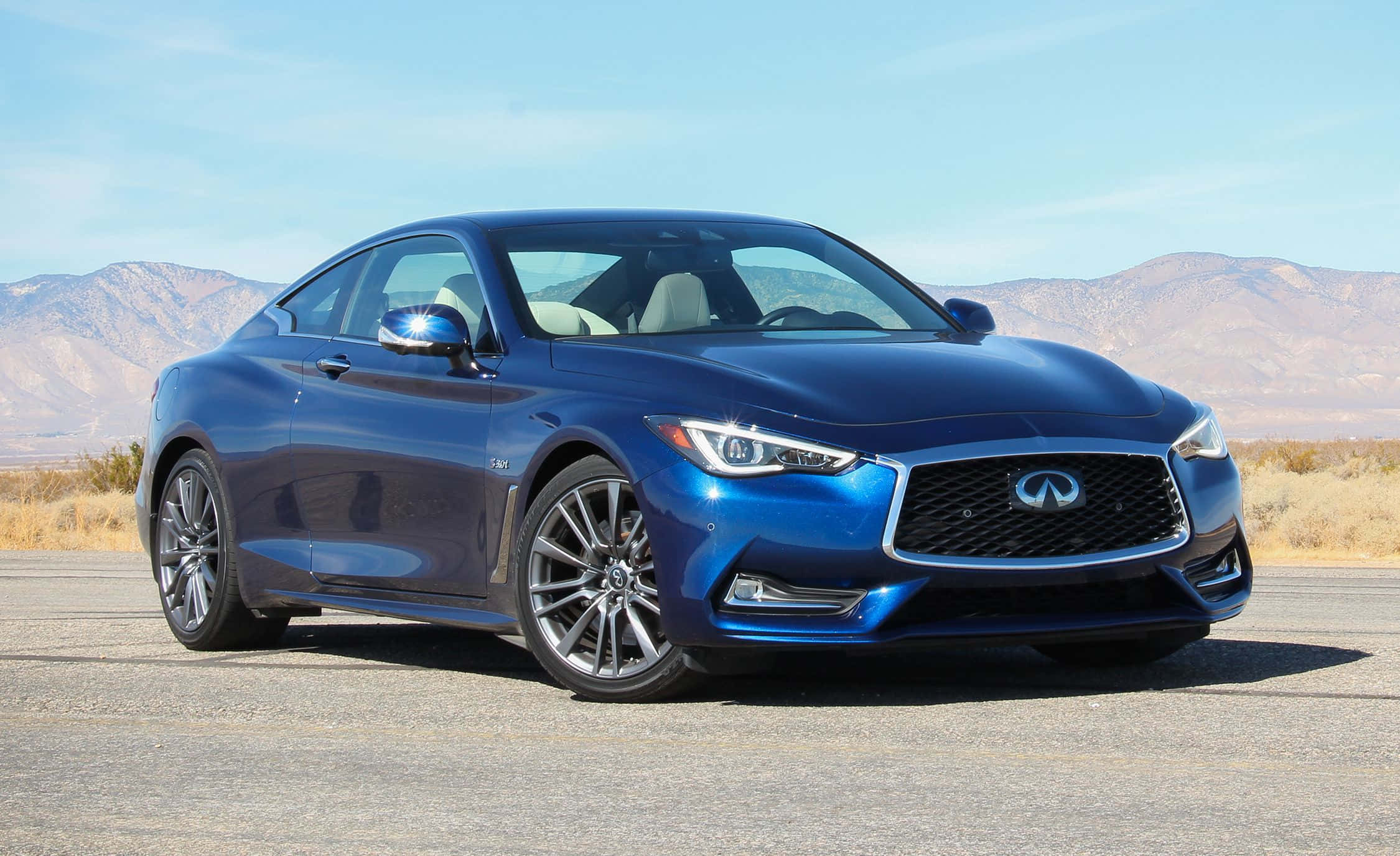 Infiniti Q60 桌布 壁紙 — 一輛時尚的藍色Infiniti Q60運動轎跑車在明亮的陽光下閃耀，背景是乾燥的沙漠山脈。