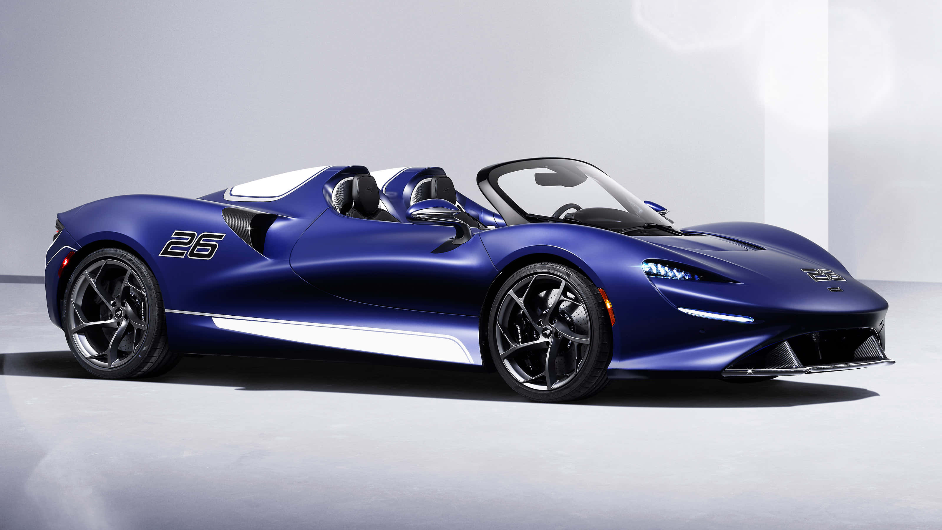 麥拉倫 桌布 壁紙 — 一輛時尚的藍色McLaren Speedtail敞篷跑車，帶有白色飾邊和黑色車輪，矗立在簡約的攝影棚環境中。