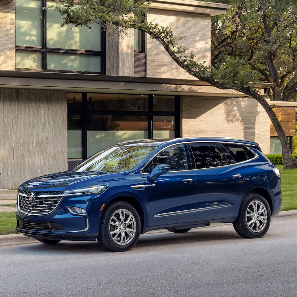 Buick 桌布 壁紙 — 一輛時尚的藍色SUV停在一條寧靜的街道上，前面是一棟帶有大窗戶和成熟樹木的現代房屋。