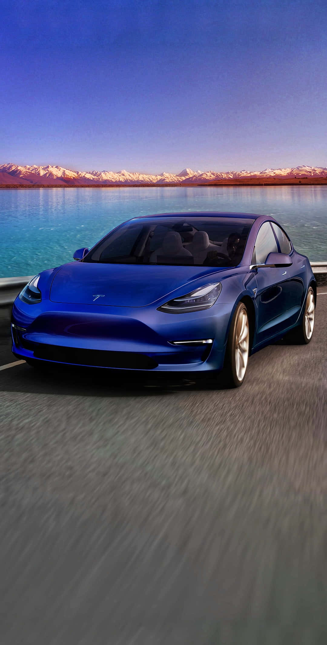 Tesla iPhone 桌布 壁紙 — 一輛時尚的藍色Tesla Model 3沿著海岸公路飛馳，背景是白雪覆蓋的山脈和碧綠的海水，天空暮色蒼茫。