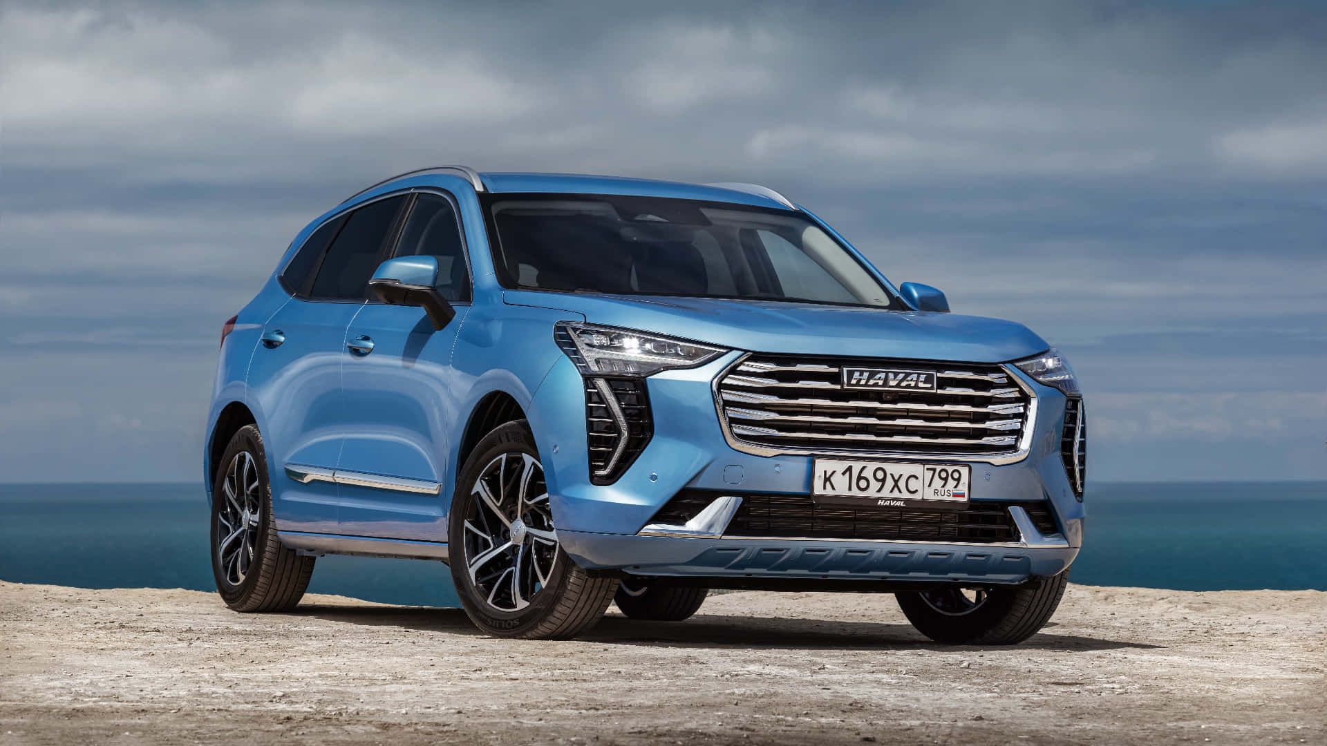Haval 桌布 壁紙 — 一輛時尚的藍色哈弗SUV停泊在岩石懸崖上，俯瞰著多雲天空下的海洋。