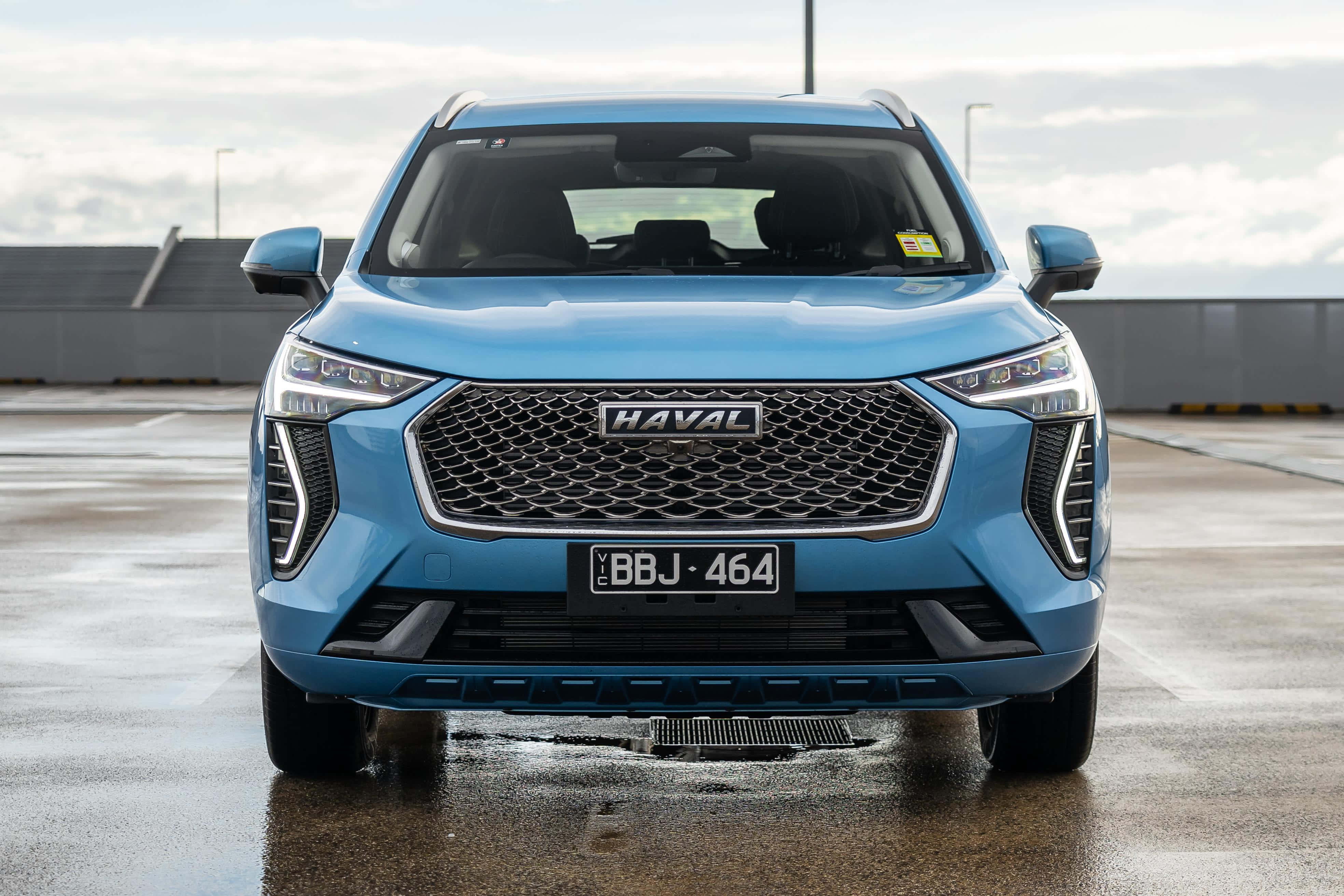 Haval 桌布 壁紙 — 一輛時尚的藍色哈弗SUV在潮濕的停車場上向前，天空陰沉，水坑反射。